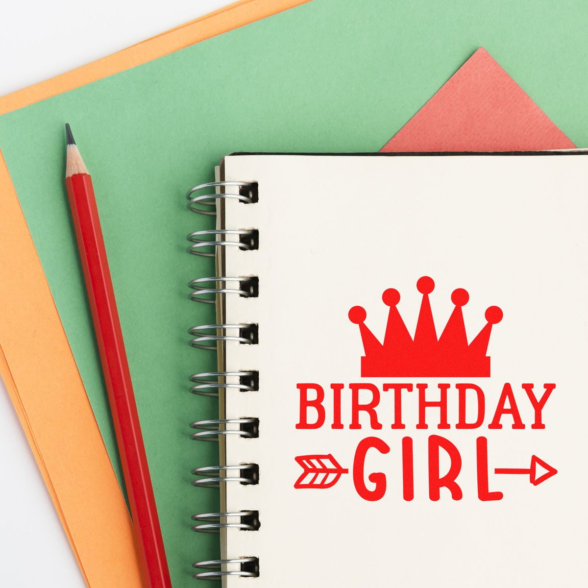 Red Birthday Girl stamp and seal on spiral notebook, with crown graphic, pencil, and green and orange paper backgrounds.