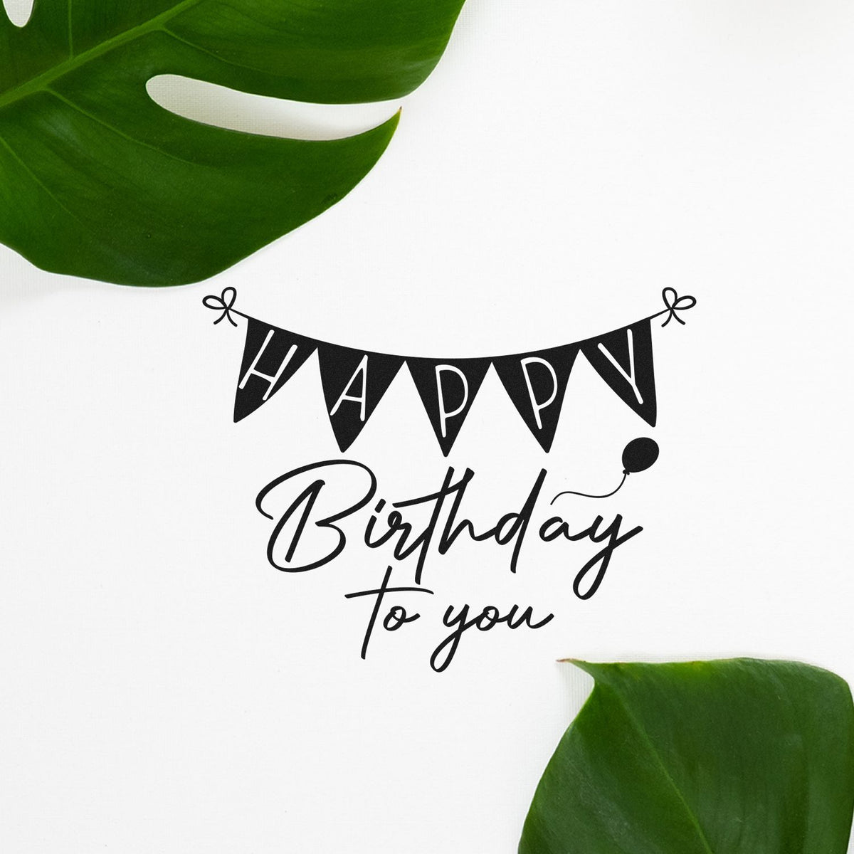 Black Happy Birthday to You stamp and seal design with bunting and balloon on white, framed by green leaves.