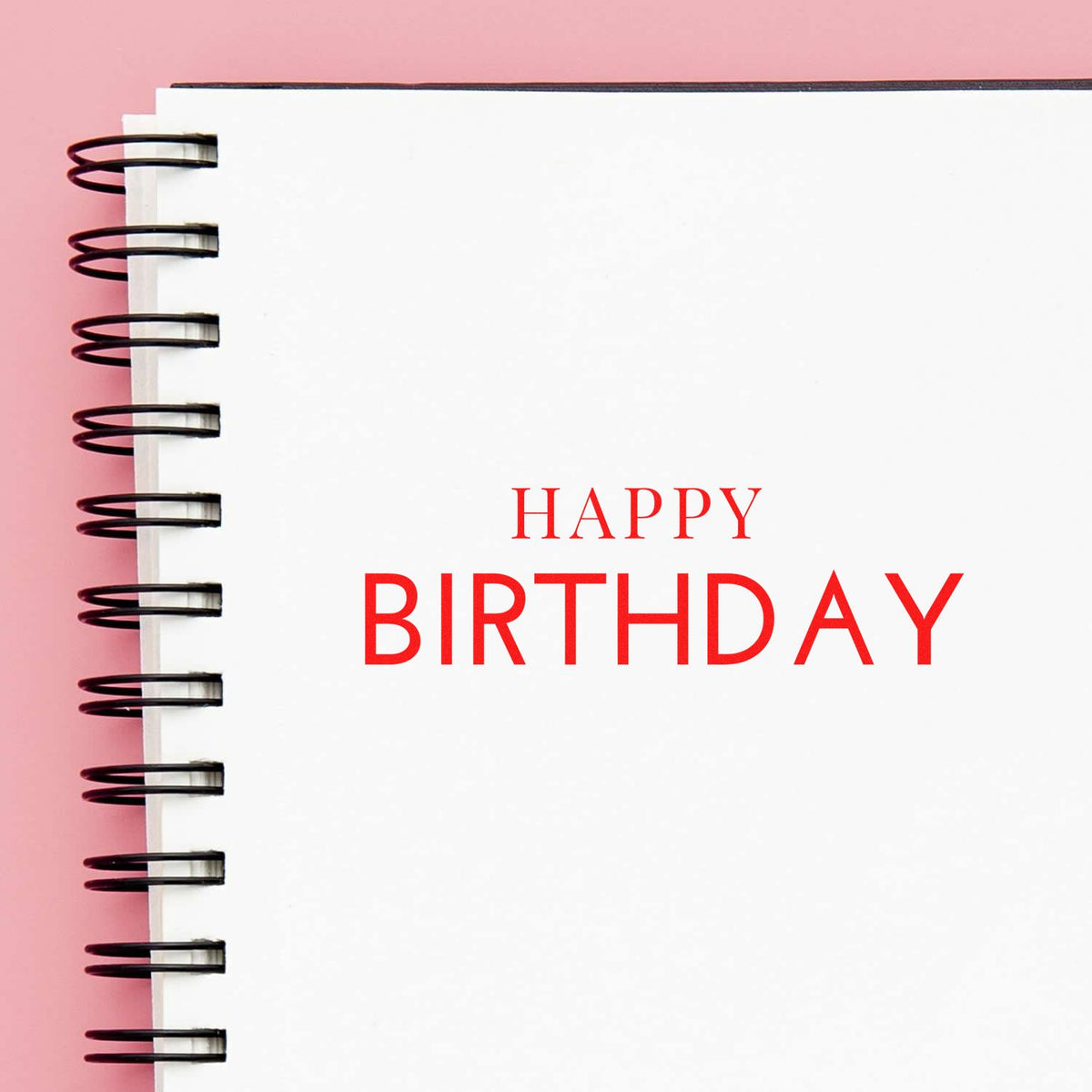 White spiral notebook with red Happy Birthday text, black binding, on pink background for stamp and seal products.