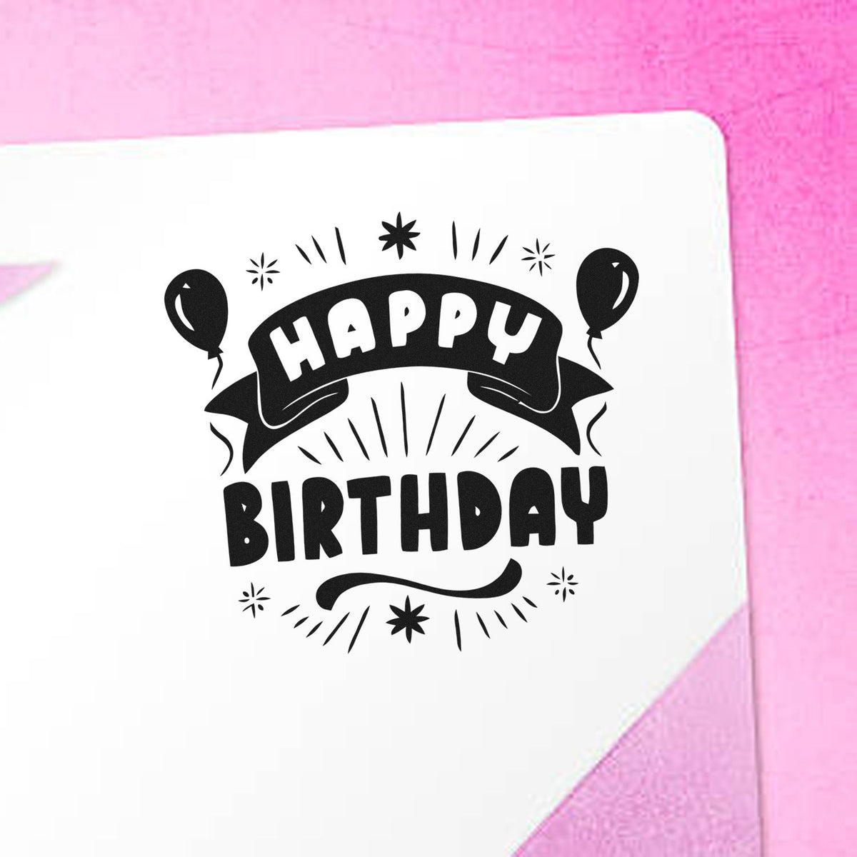 Black Happy Birthday stamp and seal with balloons on white paper against a pink background.