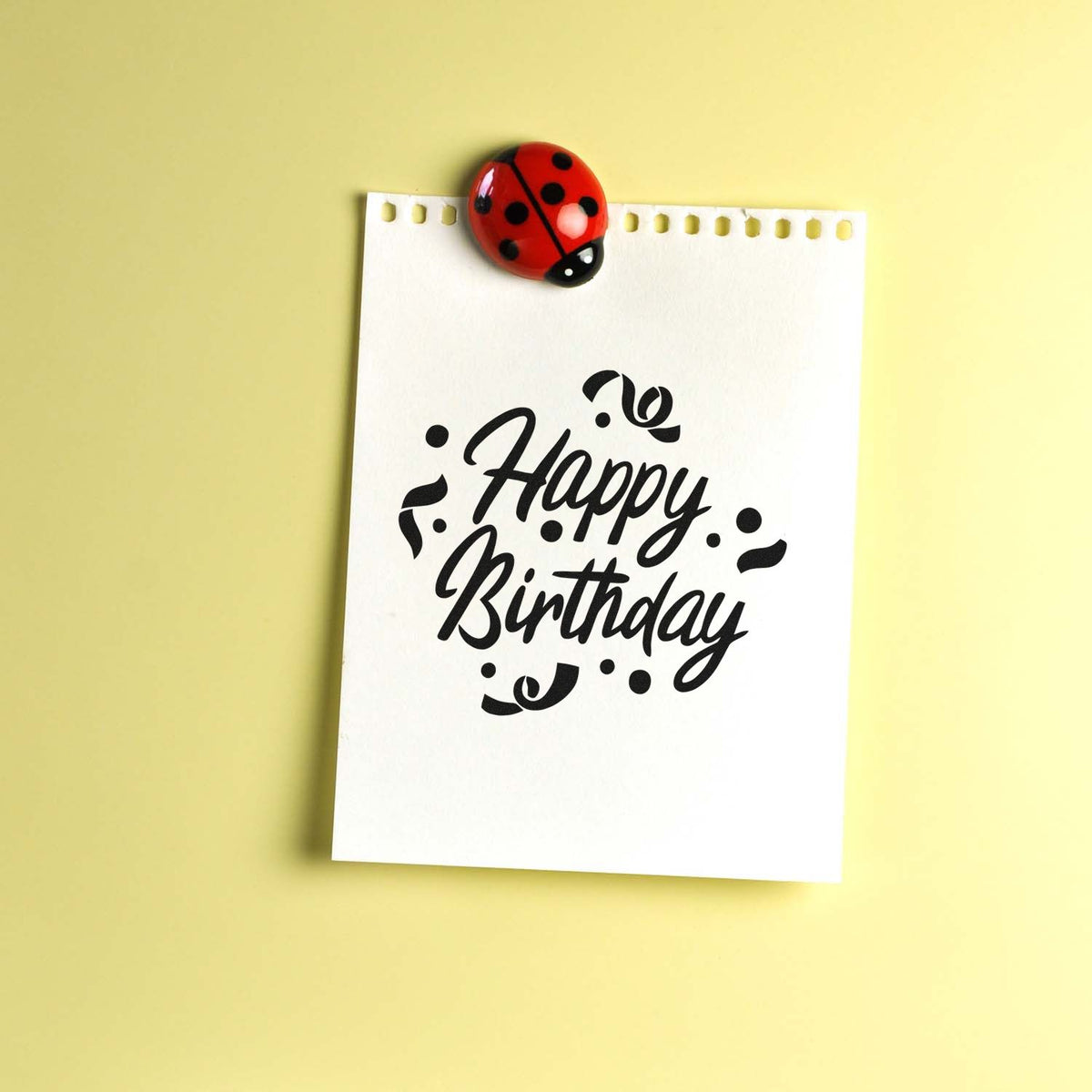 Black Happy Birthday stamp on white card, topped with a red ladybug seal, against a pale yellow background.