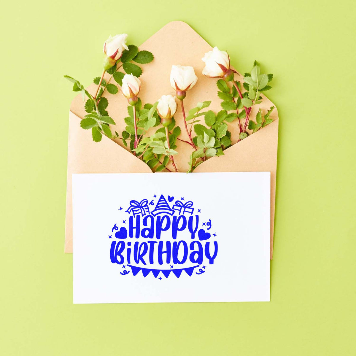 Blue Happy Birthday stamp seal on white card, tucked in a beige envelope with white roses and green leaves on lime green.