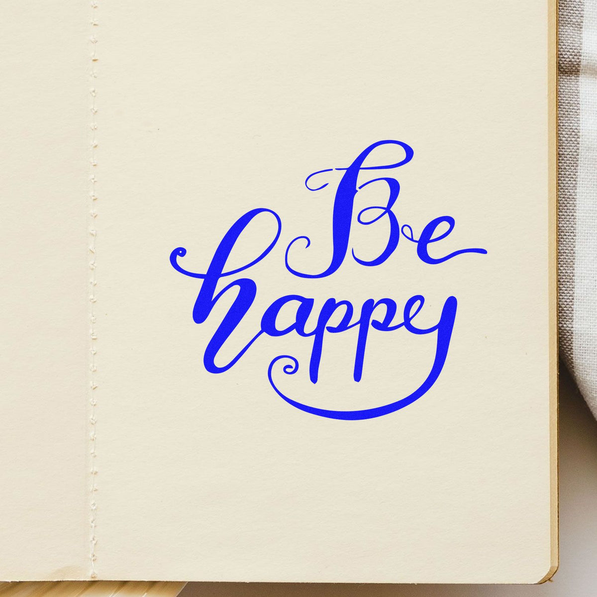 Blue Be happy calligraphy stamp seal on cream paper, with decorative swirls and bold blue script.