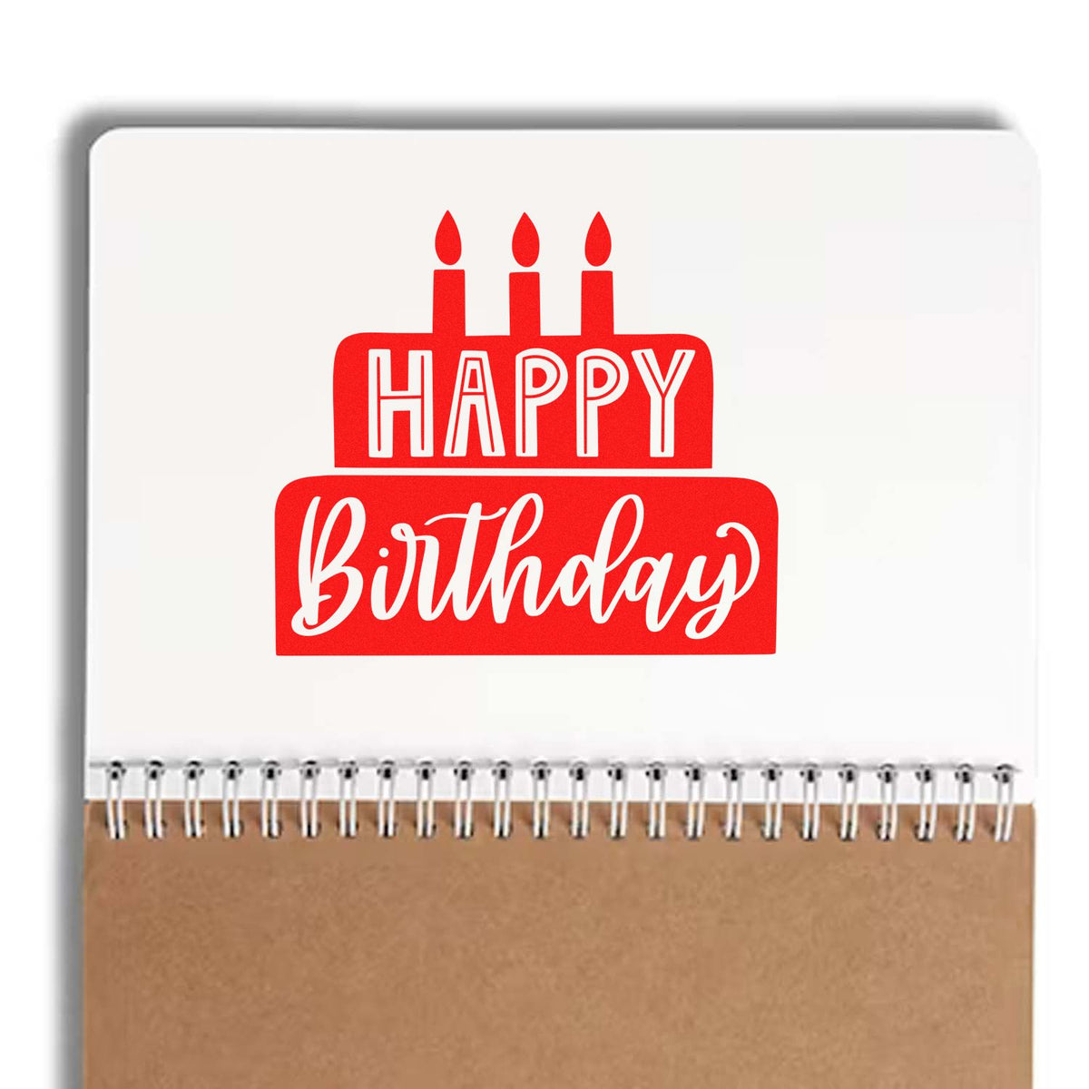 Red Happy Birthday cake stamp seal on a white spiral notebook with kraft cover and silver binding.