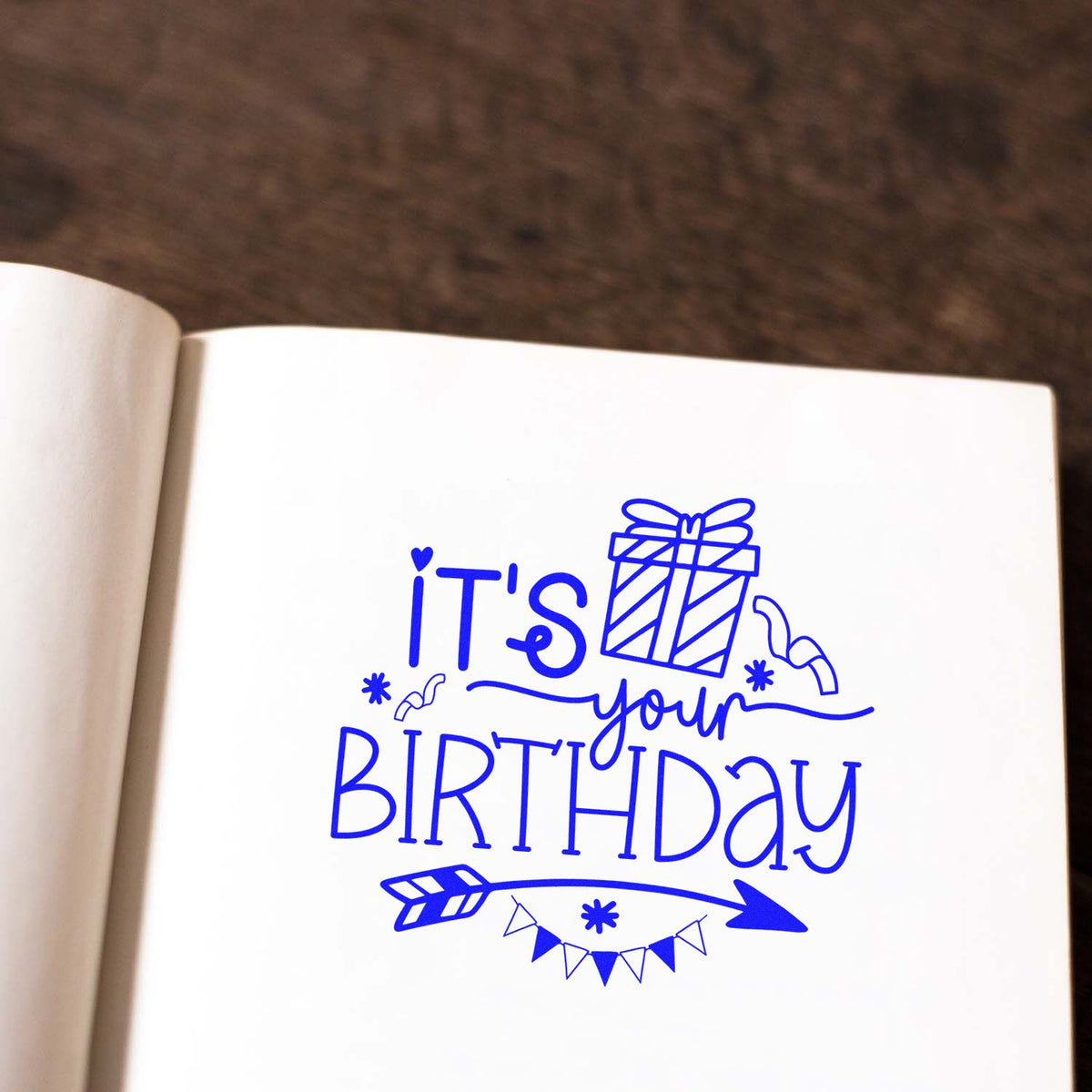 Blue birthday stamp and seal design on white paper, featuring a gift, arrow, bunting, and the words Its your birthday