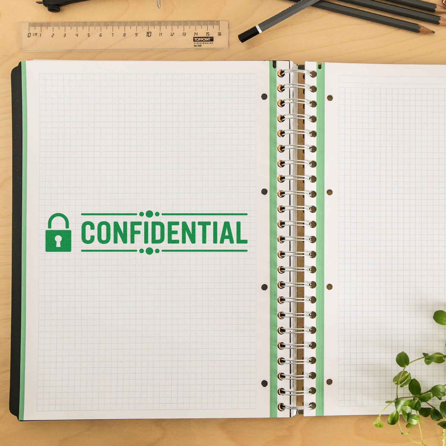 Green confidential stamp on open spiral notebook with grid paper, on a desk with ruler and pencils for seal and stamp products.