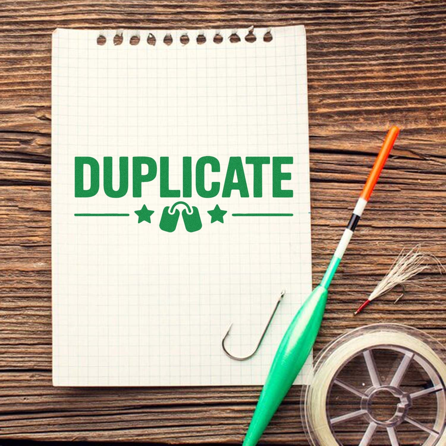 Green DUPLICATE stamp seal on graph paper notebook, with embossing tool and clear tape on a rustic wood desk.