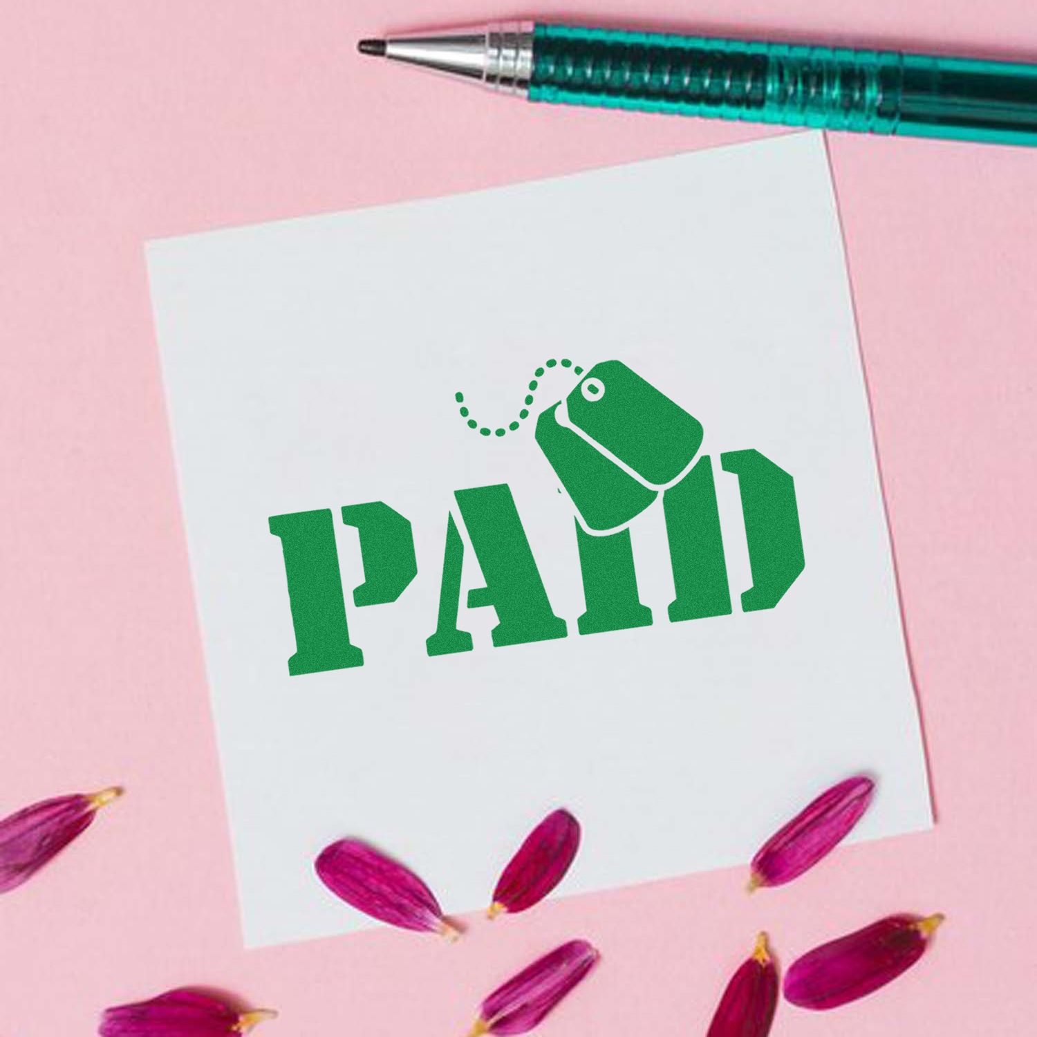 Green PAID rubber stamp seal on white card with teal pen, on a pink background with magenta petals.