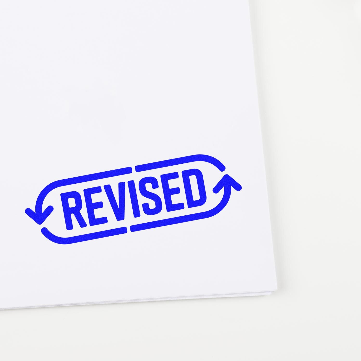 Blue REVISED stamp seal with curved arrows on white paper, marking document approval.