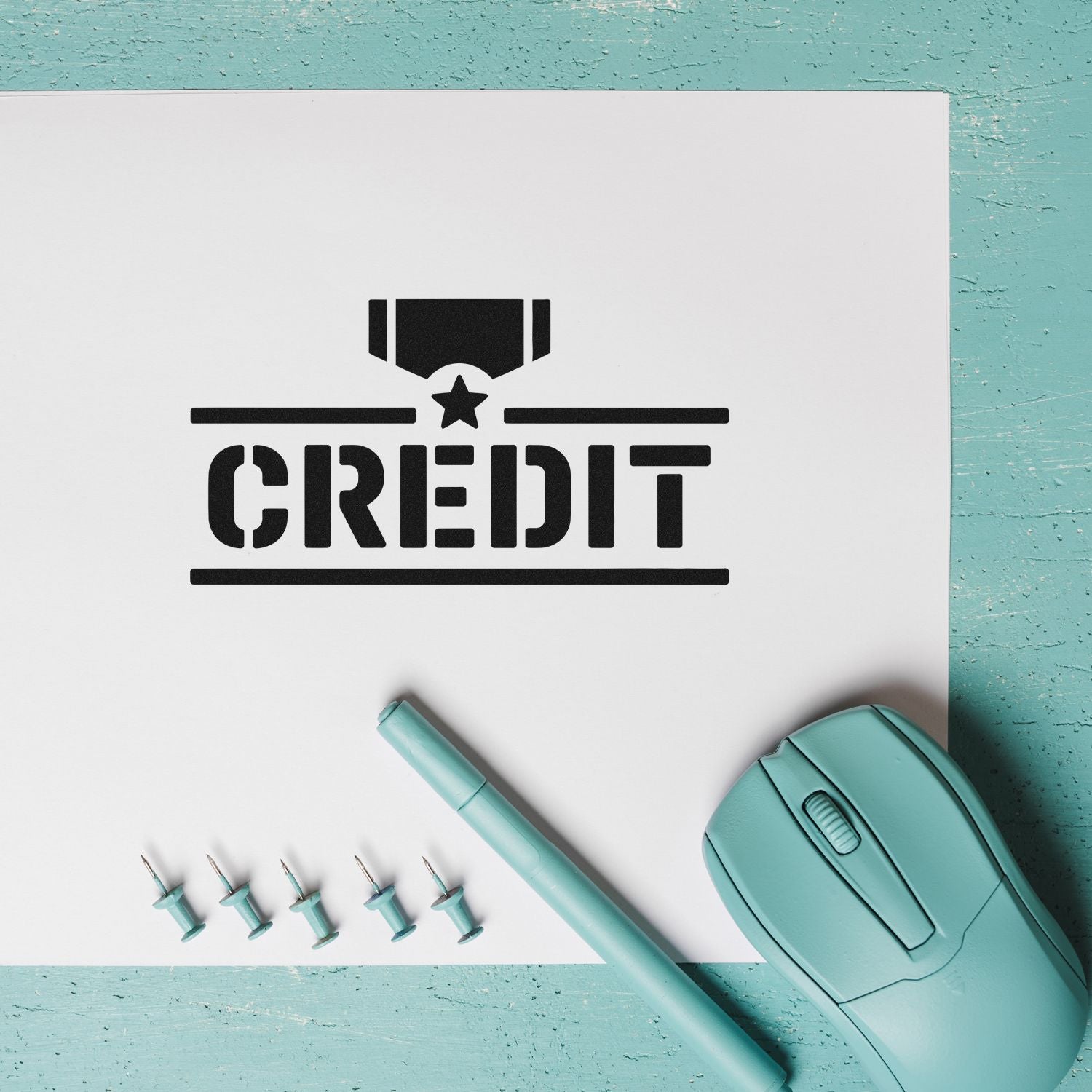 Black CREDIT stamp and seal on white paper, with teal stamp tool, pen, and pins on a turquoise background.