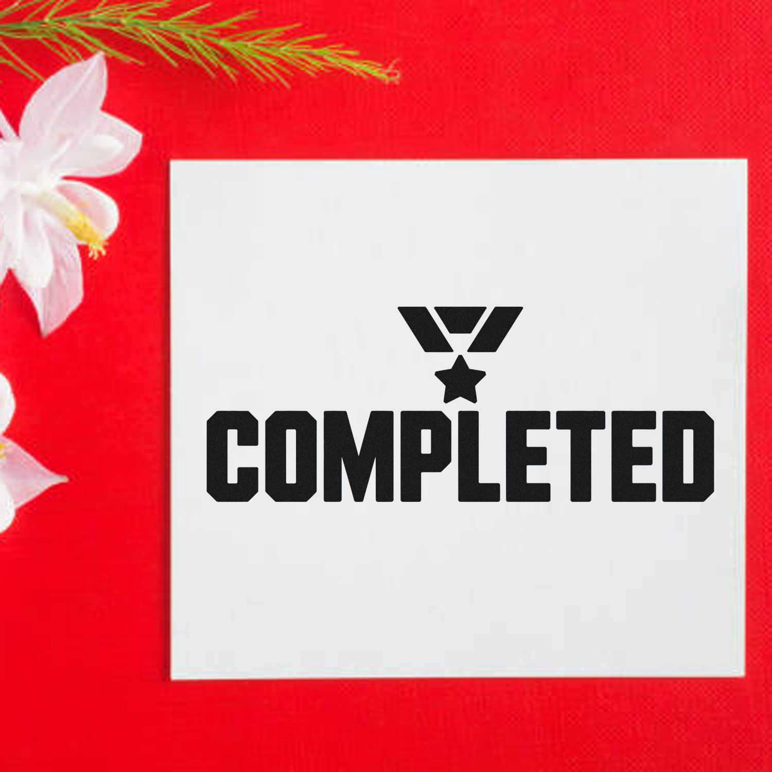 White square self-inking stamp with black COMPLETED seal on red background, accented by white flowers and greenery.