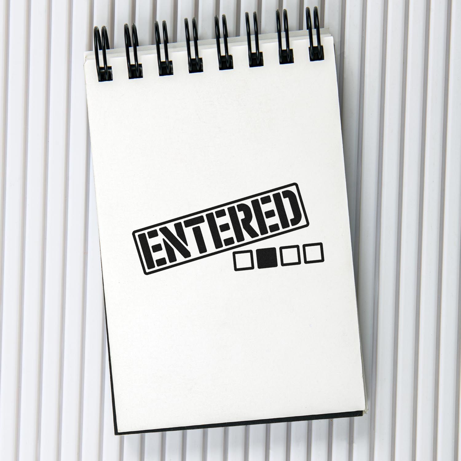 Black ENTERED stamp seal on white spiral notepad with small checkbox squares.