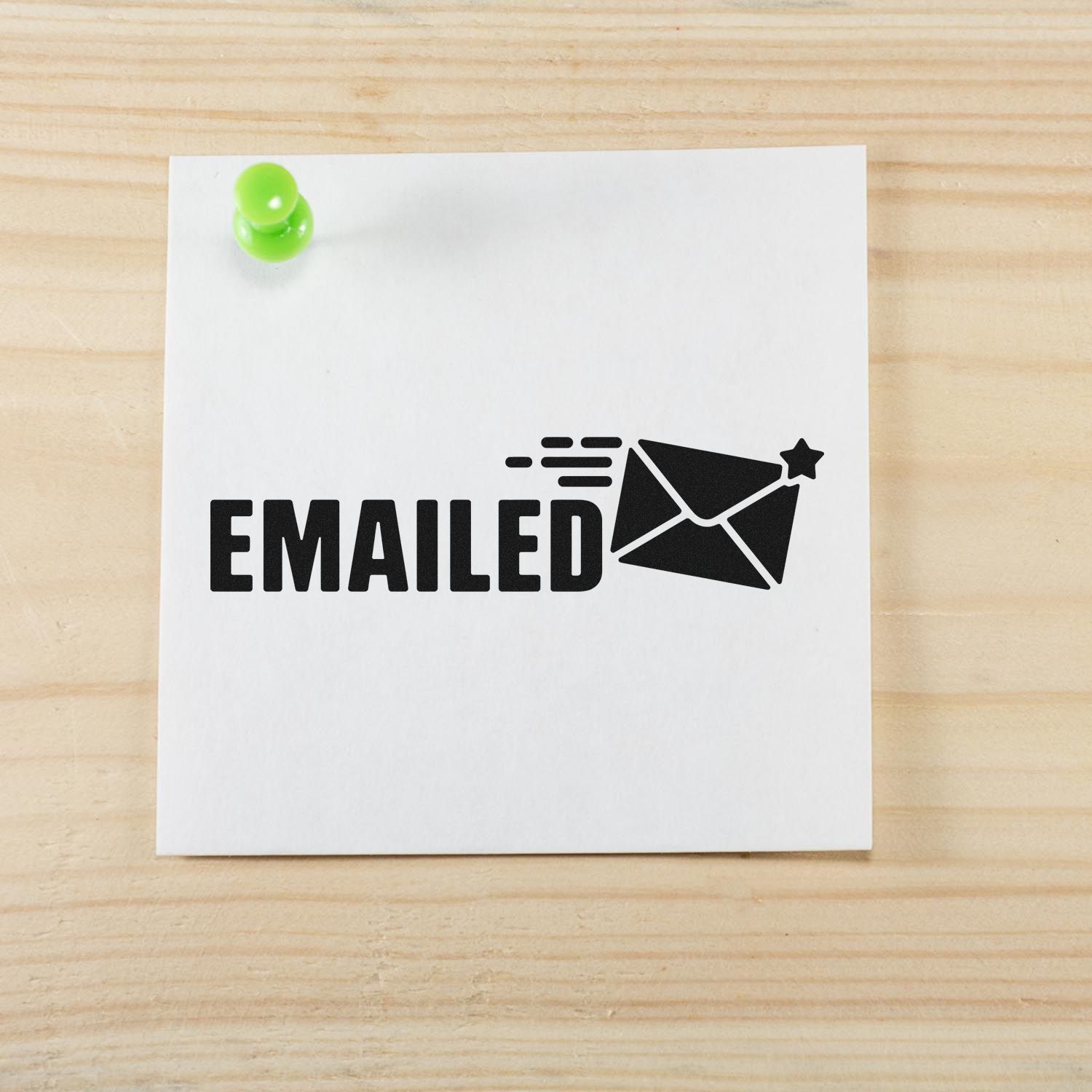 Black EMAILED rubber stamp seal with envelope icon on white paper, pinned by a bright green pushpin on light wood.