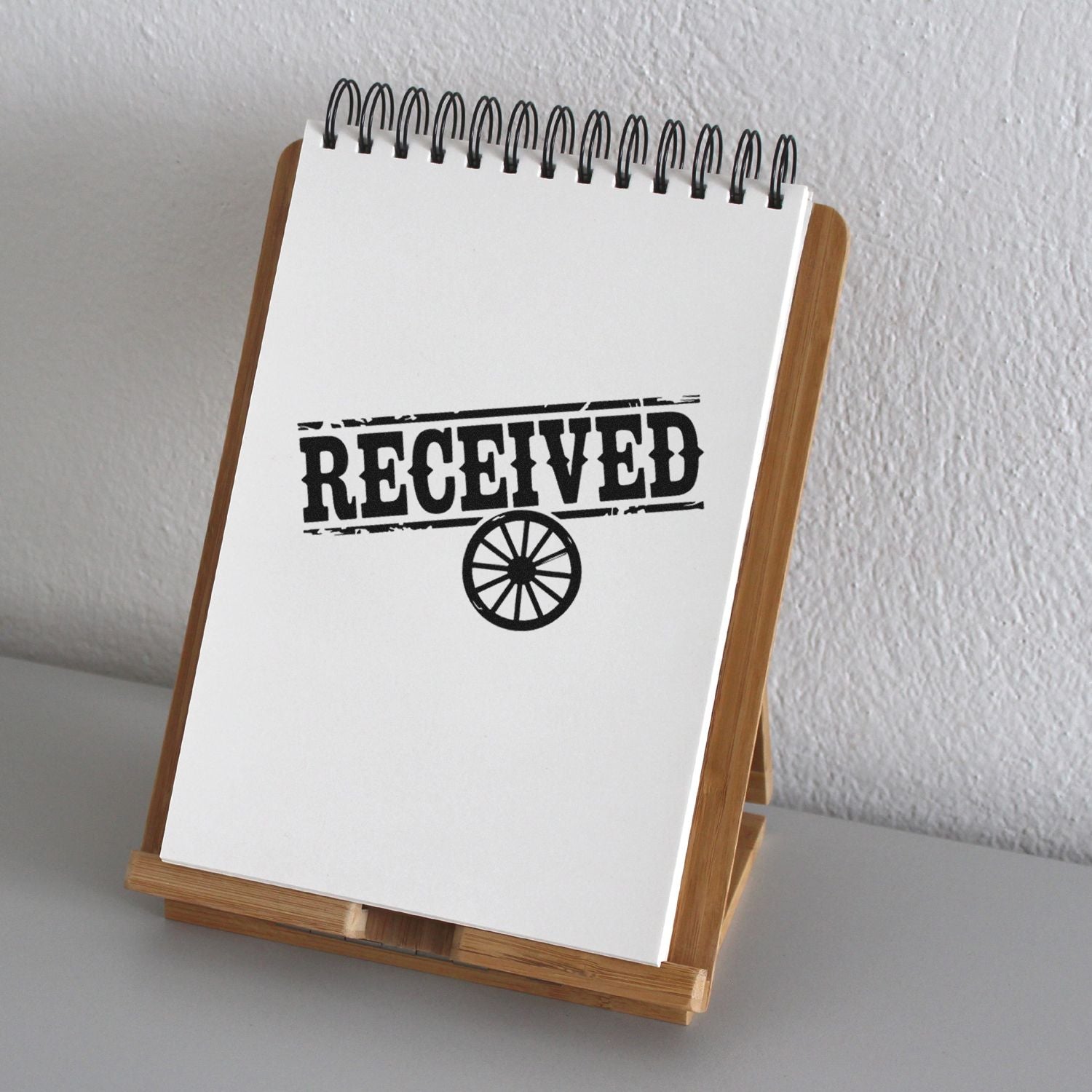 Black RECEIVED rubber stamp with wheel seal on white spiral notepad in a wooden stand.