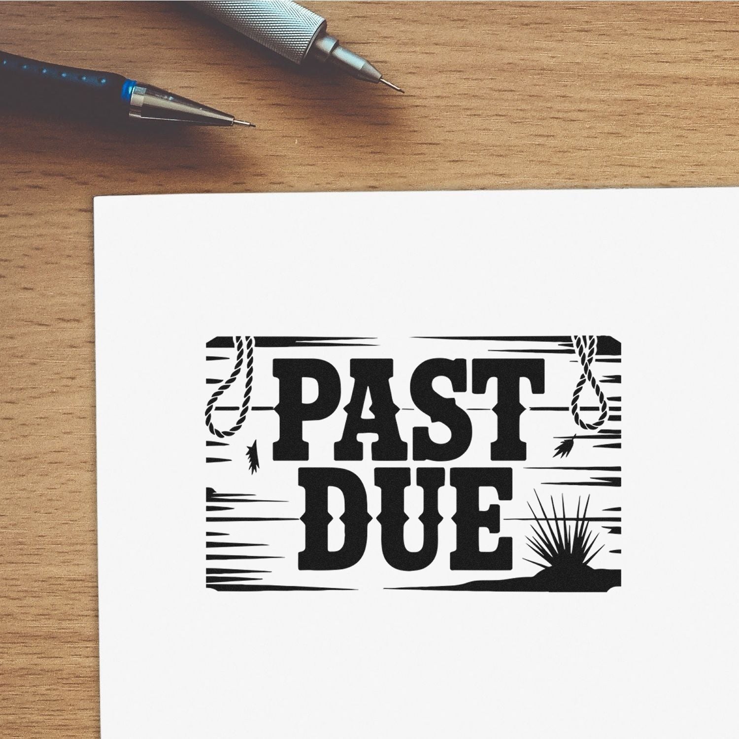 Black PAST DUE stamp and seal design on white paper, with distressed rope and sunburst accents beside pens on a wood desk.