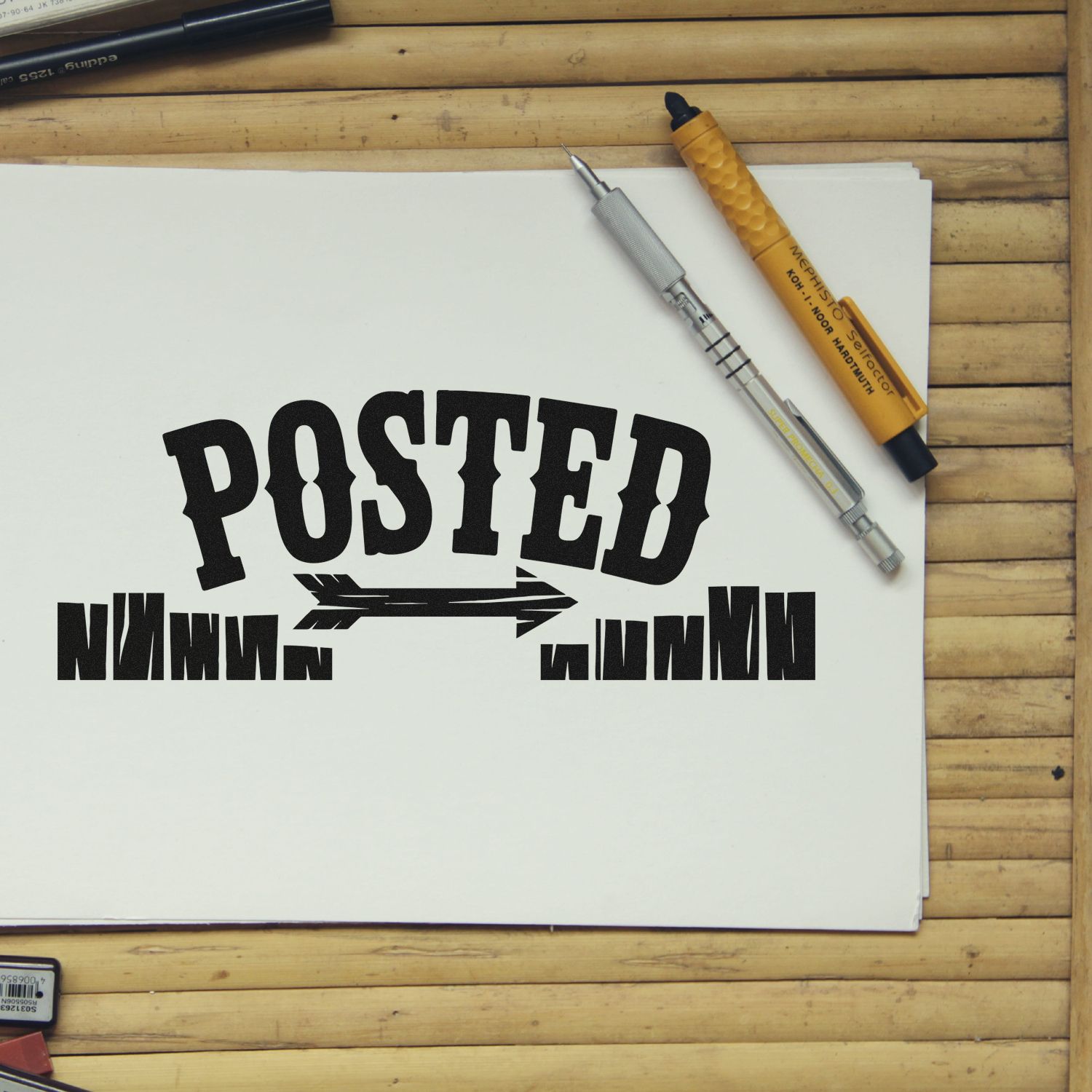 Black POSTED stamp and seal design on white paper with silver and yellow stamp tools on a wooden desk.