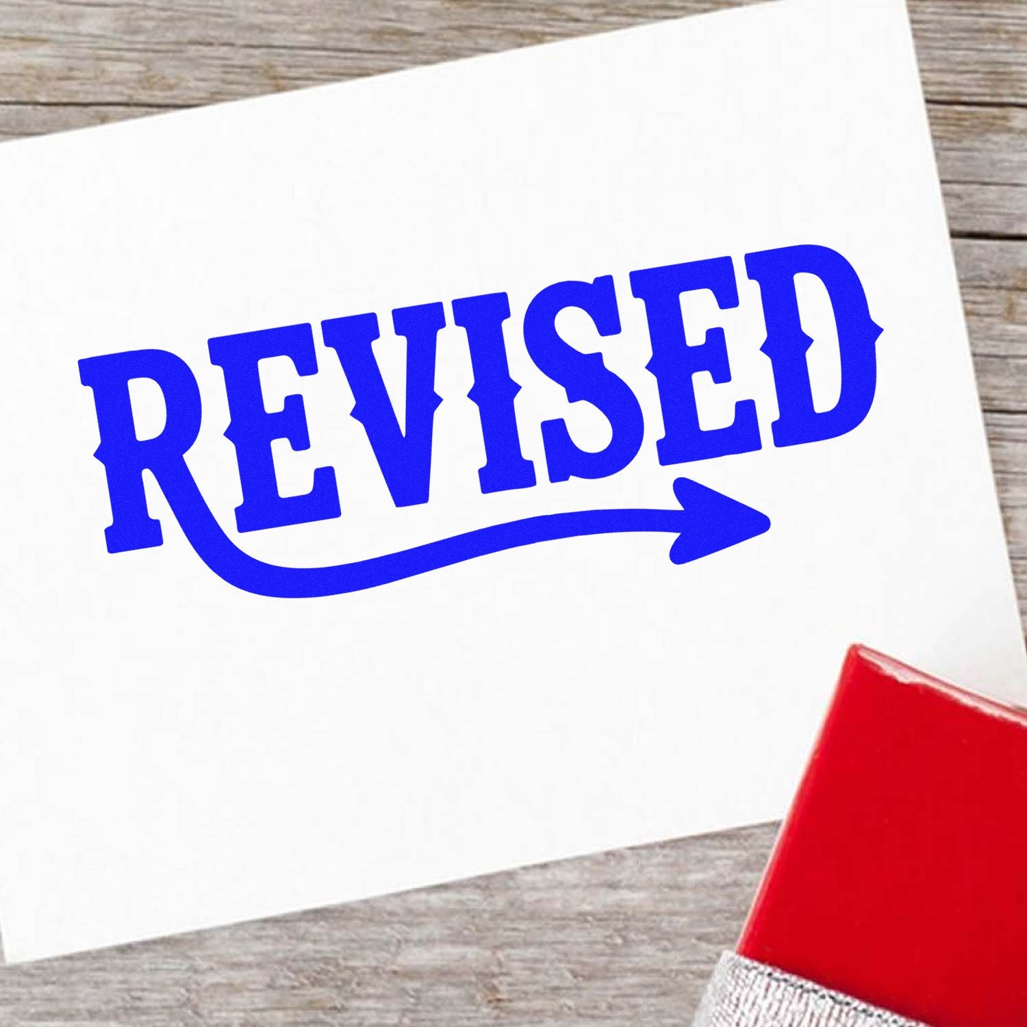 Blue REVISED rubber stamp imprint on white paper beside a red ink pad, showing stamp and seal products.