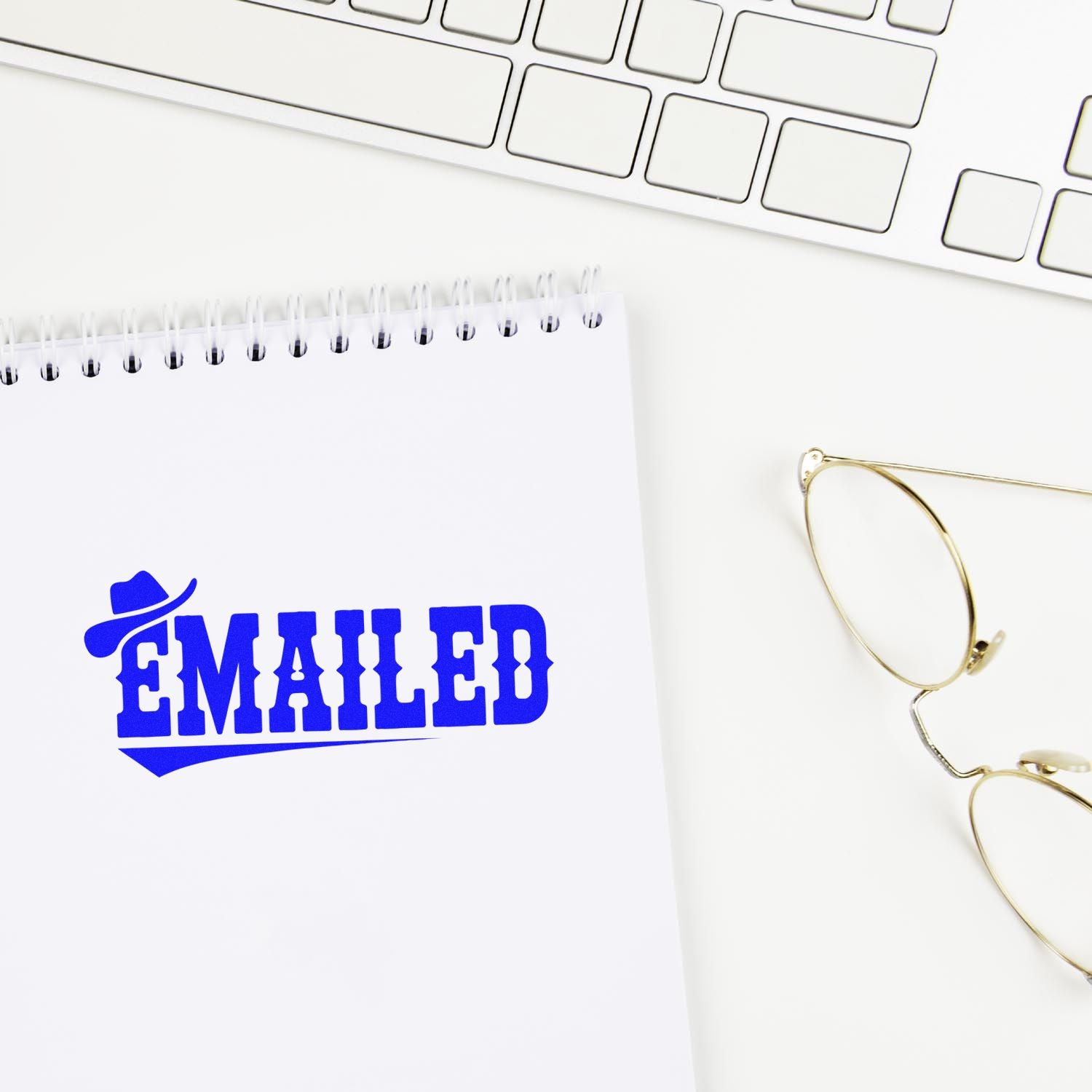 Blue EMAILED rubber stamp on a white spiral notebook beside a keyboard and gold glasses, showcasing stamp and seal products