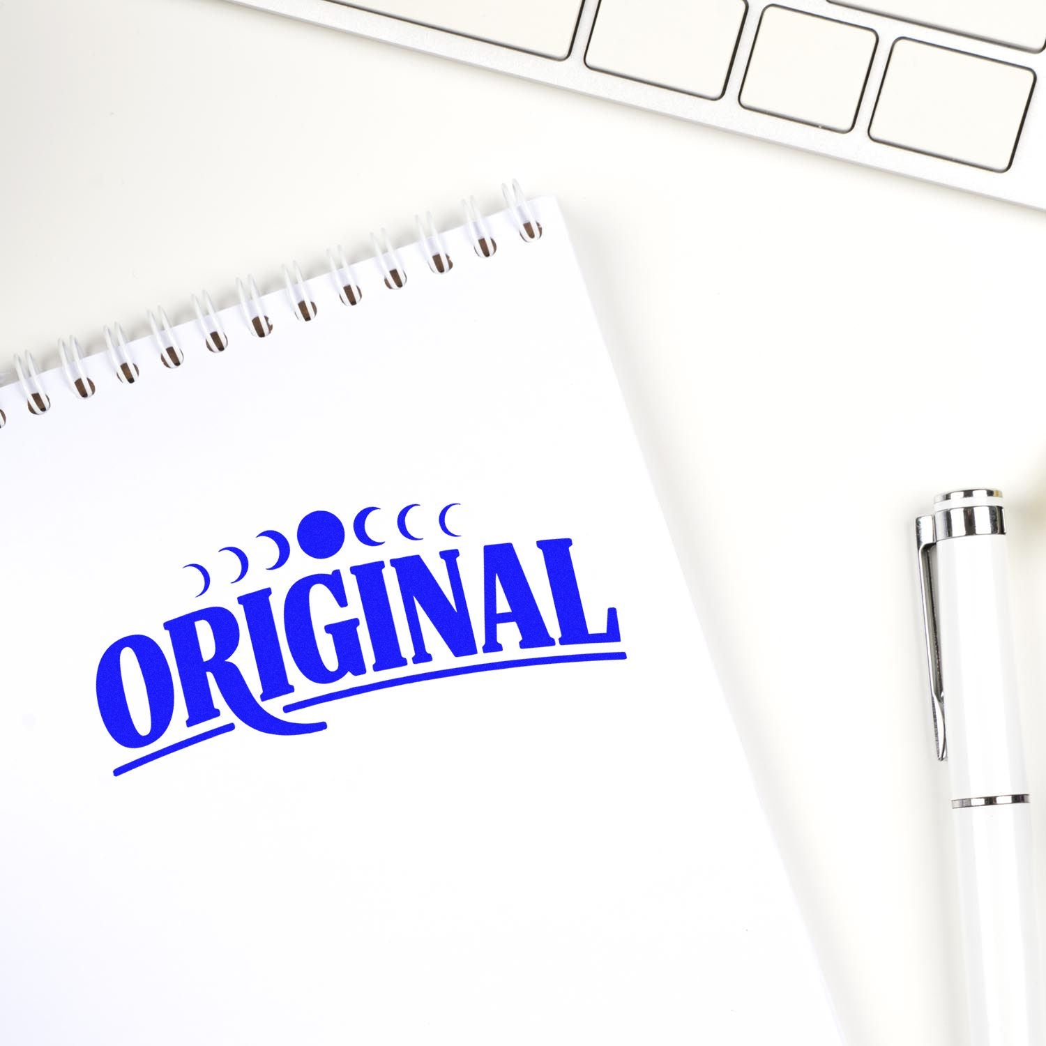 Blue ORIGINAL stamp on white spiral notebook beside a white pen, highlighting stamp and seal products.