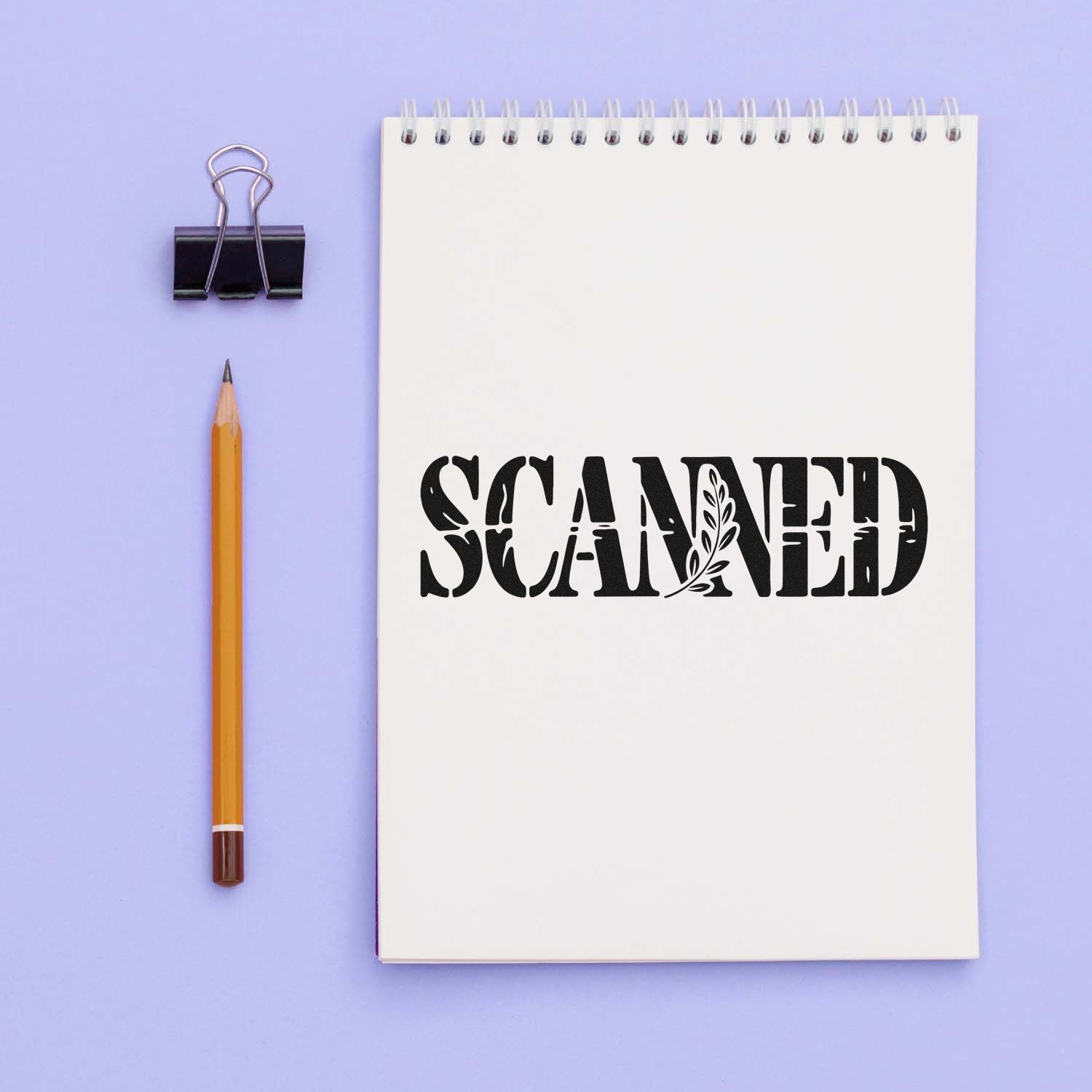 White spiral notebook with bold black SCANNED seal stamp, binder clip, and pencil on a lavender background.