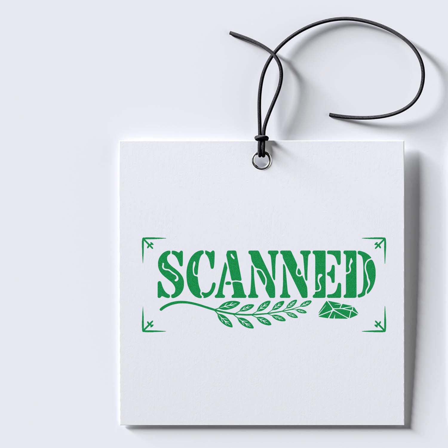 White hanging tag with black cord, featuring a green SCANNED stamp seal, leaf graphic, and corner marks.