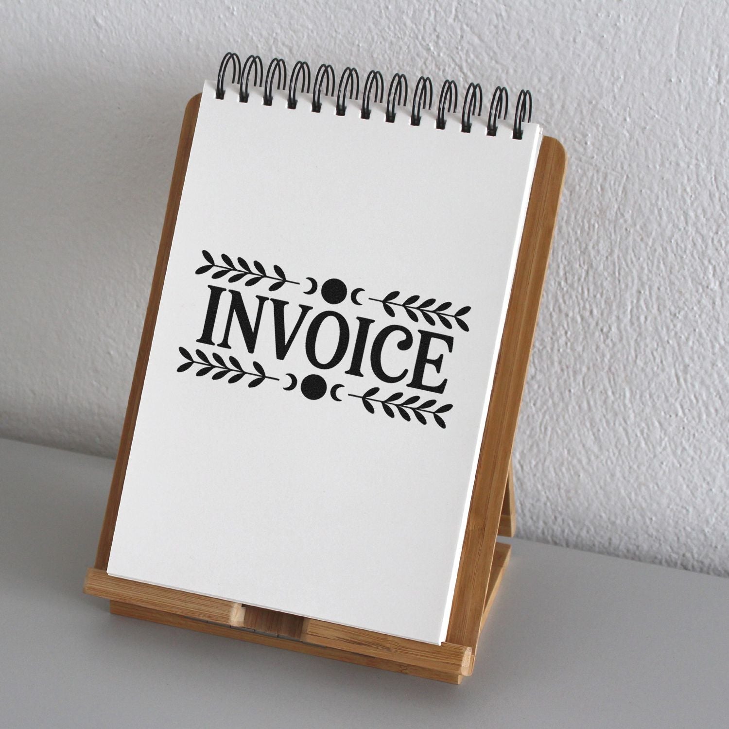 Black invoice stamp and seal design on a white spiral notepad in a wooden display stand.