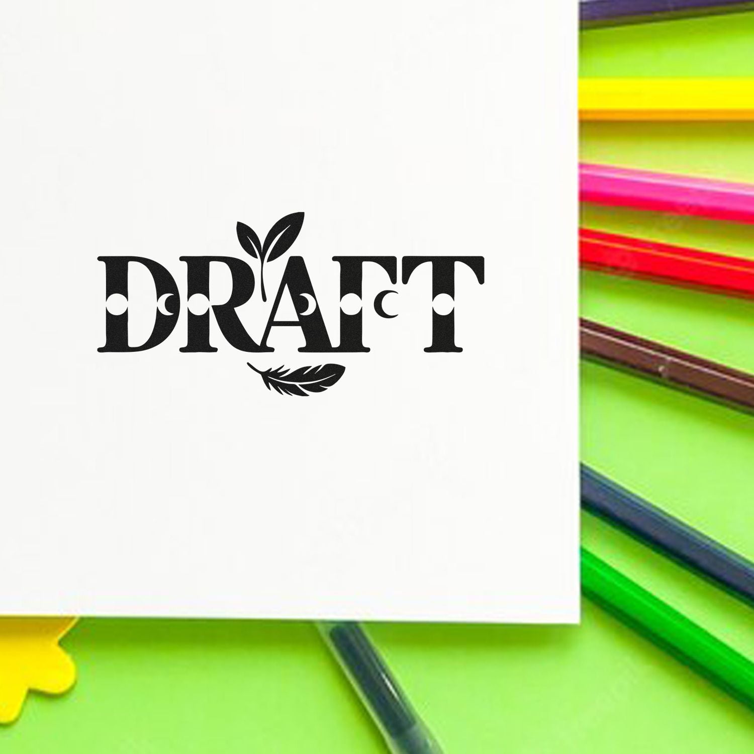 Black DRAFT stamp/seal with leaf accents on white paper, surrounded by bright green, yellow and pink pencils.