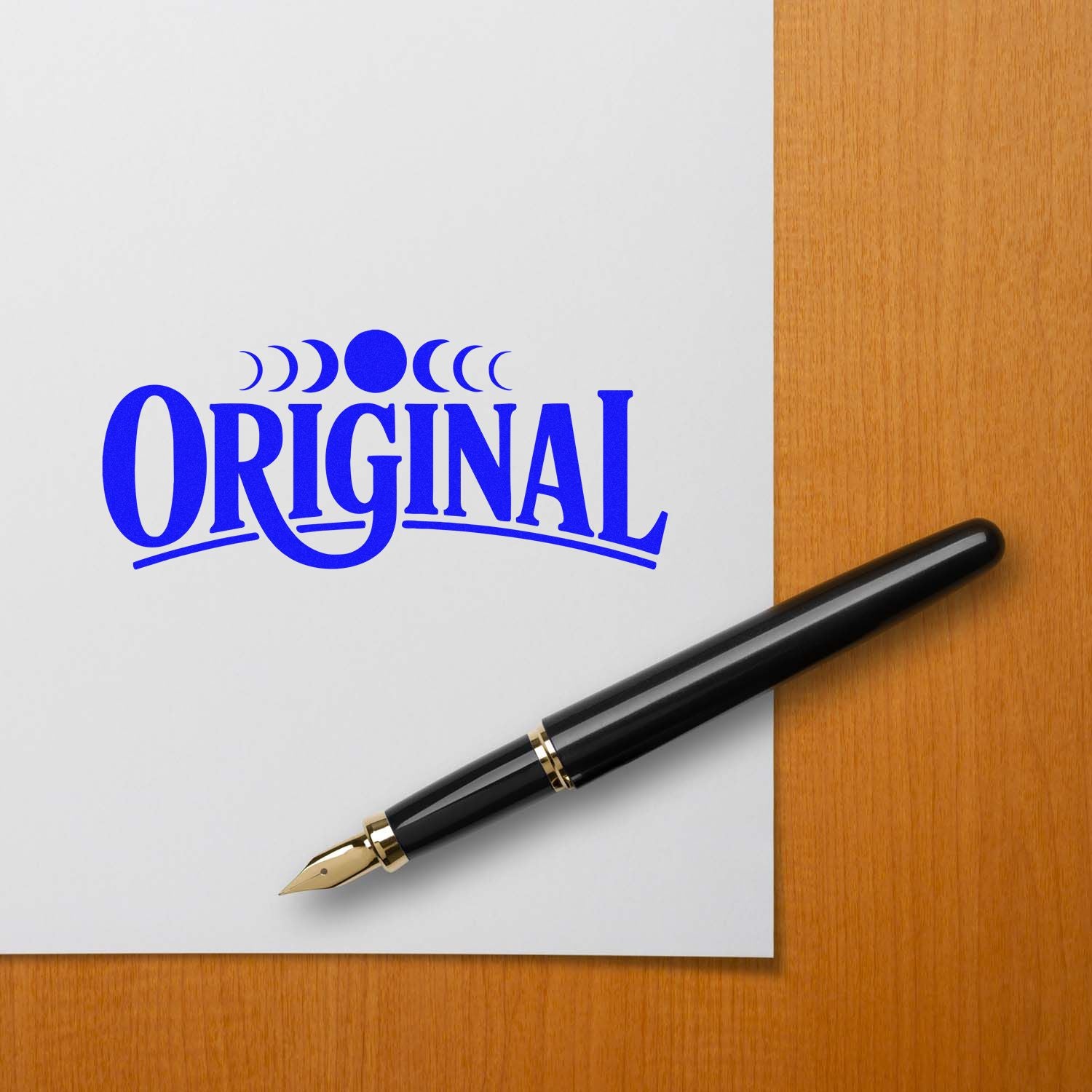 Blue ORIGINAL stamp seal with crescent accents beside a black fountain pen on white paper over a wood desk
