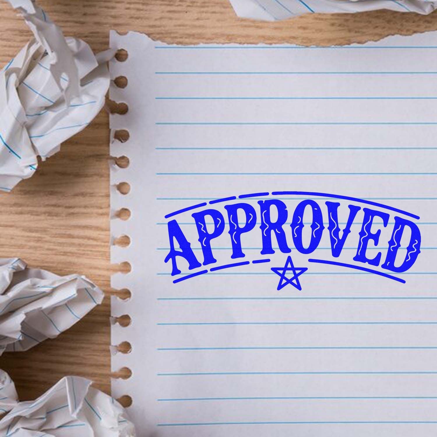 Blue APPROVED rubber stamp seal on torn lined notebook paper over a wooden desk, with crumpled paper edges.