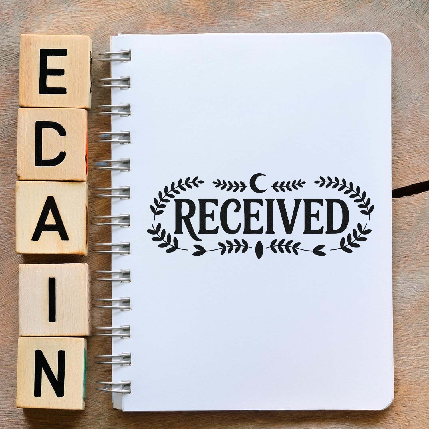 Wooden alphabet stamp blocks next to a white spiral notebook stamped RECEIVED in black with decorative leaf seal.