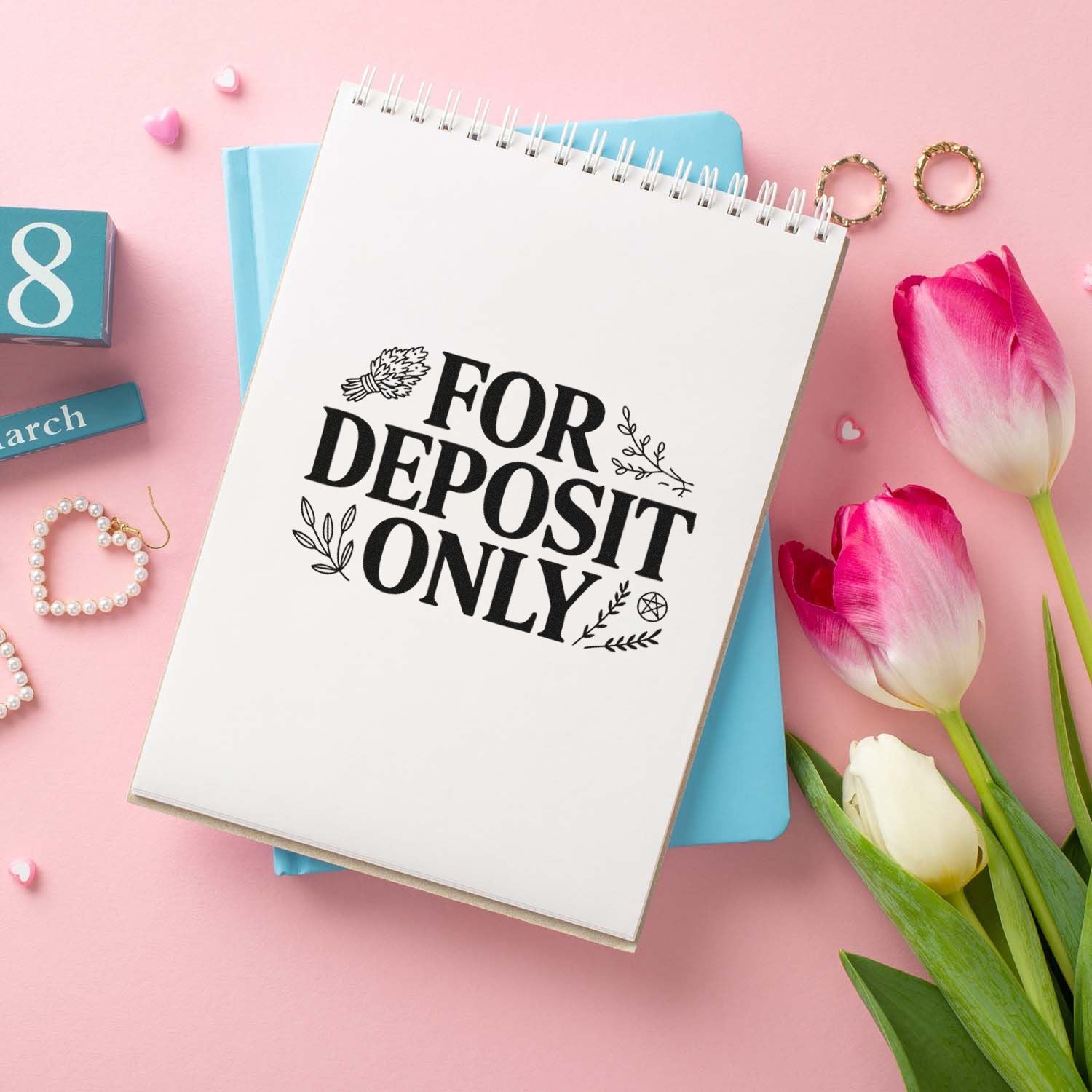 White spiral notebook with black For Deposit Only stamp, on pink background with blue paper, tulips, and gold rings.