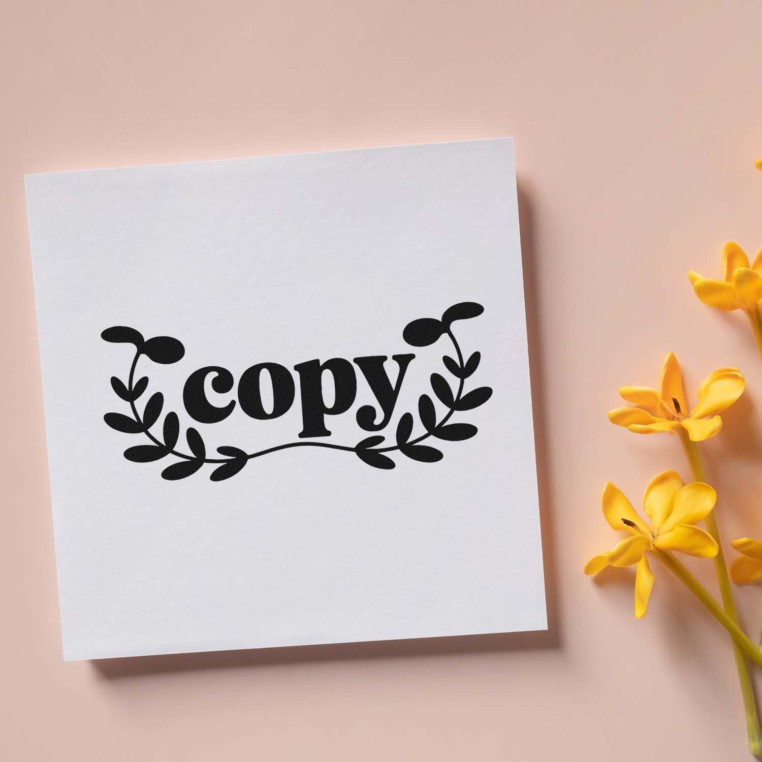 White square card with black copy stamp seal and leafy wreath on pale pink background, accented by yellow flowers.