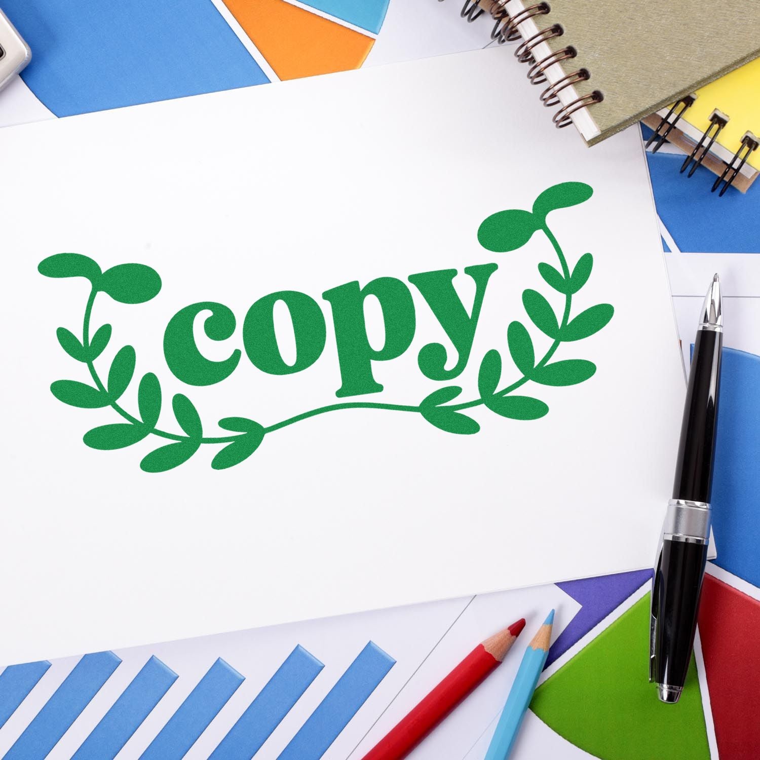 Green copy seal stamp with leafy wreath on white paper, surrounded by colorful notebooks, pens, and envelopes.