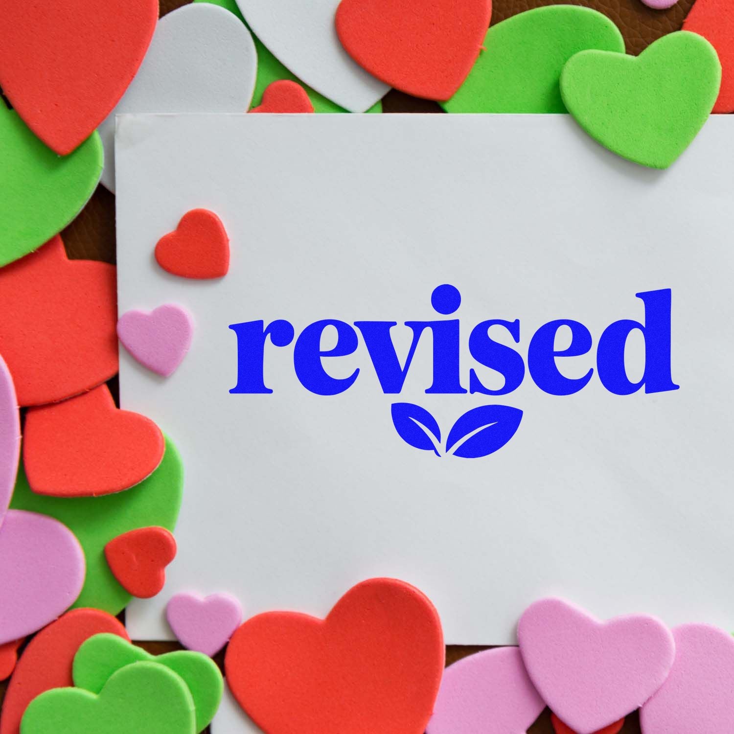 Blue revised stamp with leaf seal on white card, surrounded by red, pink, and green heart-shaped seals.
