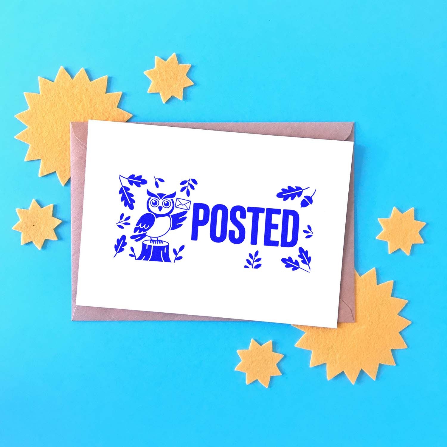Blue POSTED stamp with owl and leaves on white card over mauve envelope, on bright blue background with yellow starburst seals