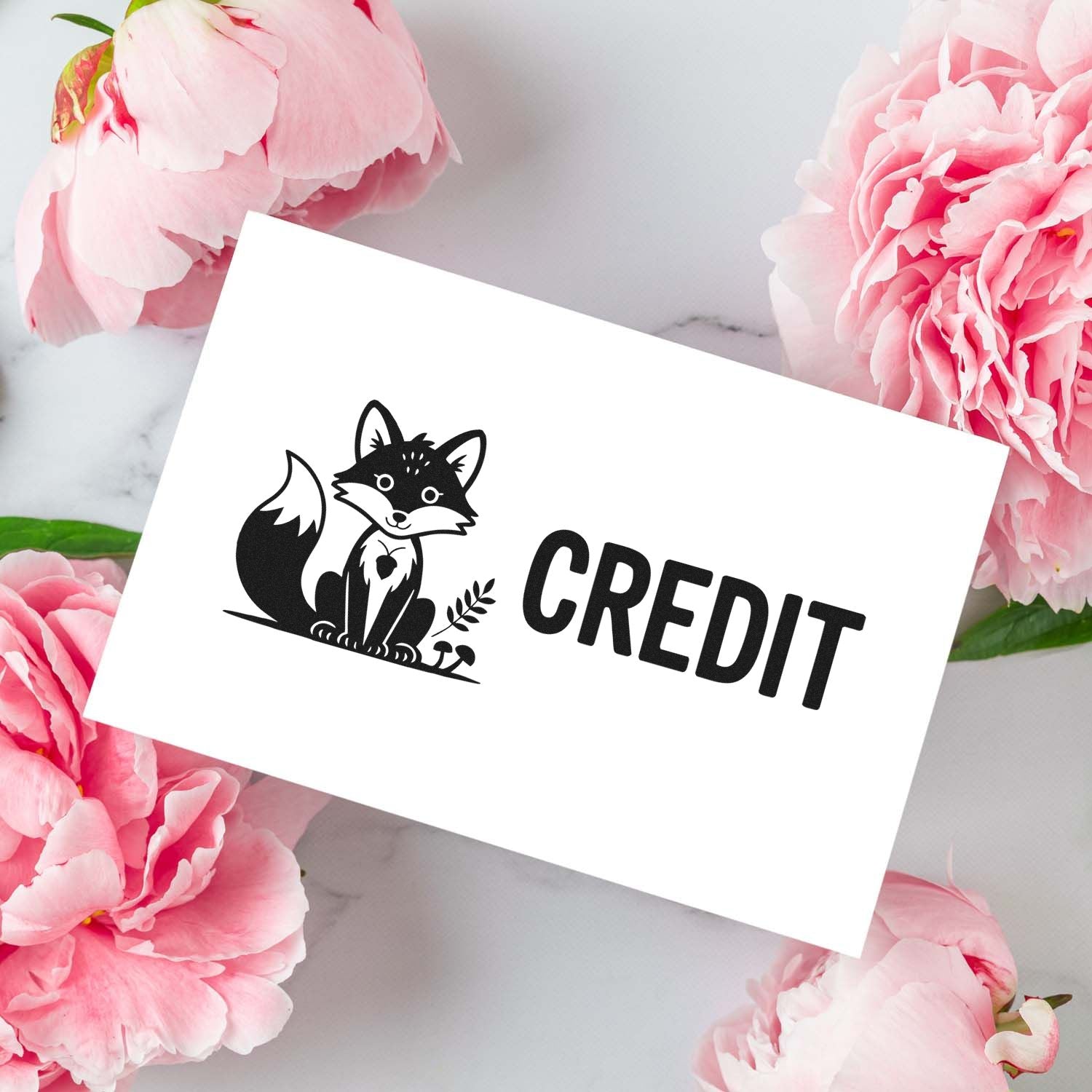 Black fox CREDIT stamp seal on white card, surrounded by pink peonies on a light marble background