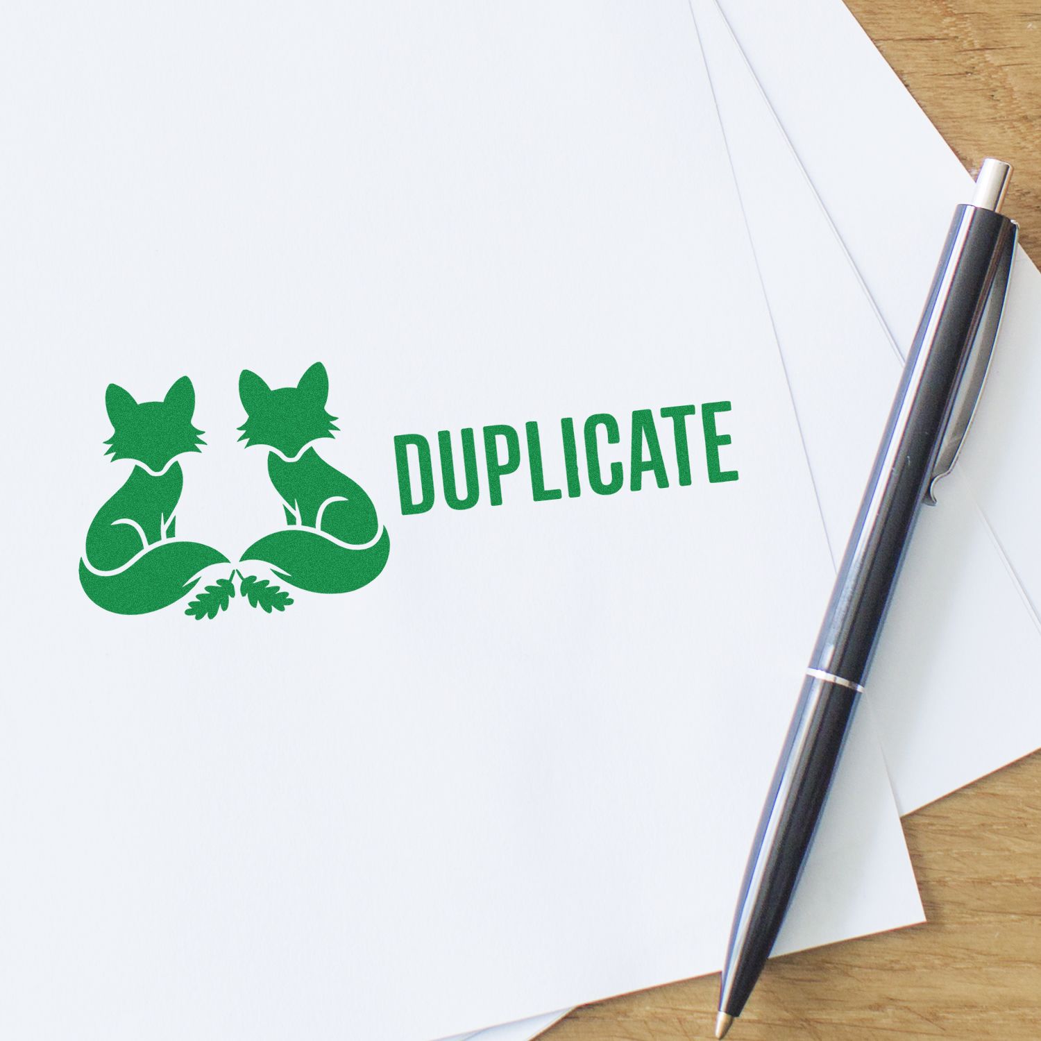 Green duplicate stamp seal with two fox silhouettes on white paper, beside a black pen on a wood desk.