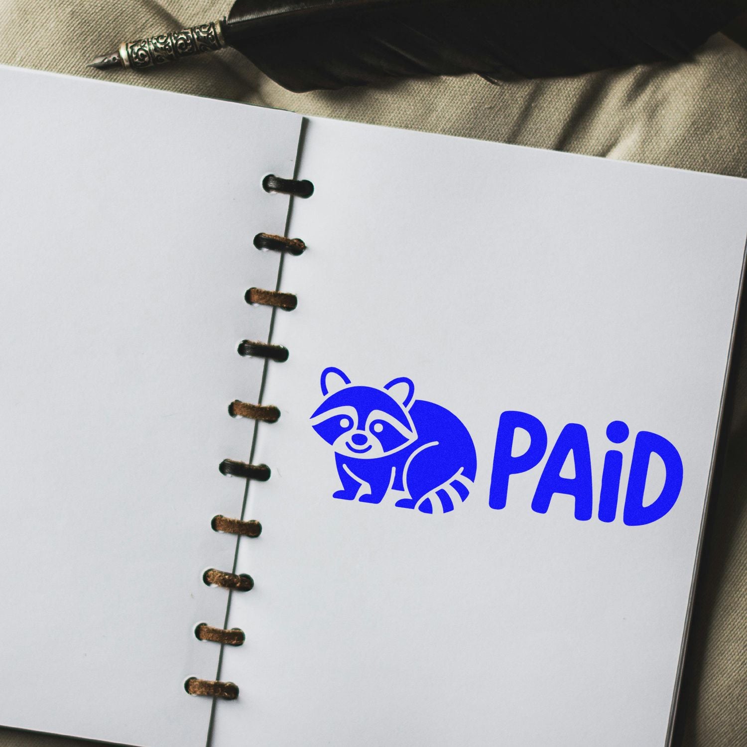 Blue PAID stamp with raccoon icon on a white notebook page, showing a seal impression beside dark spiral binding.