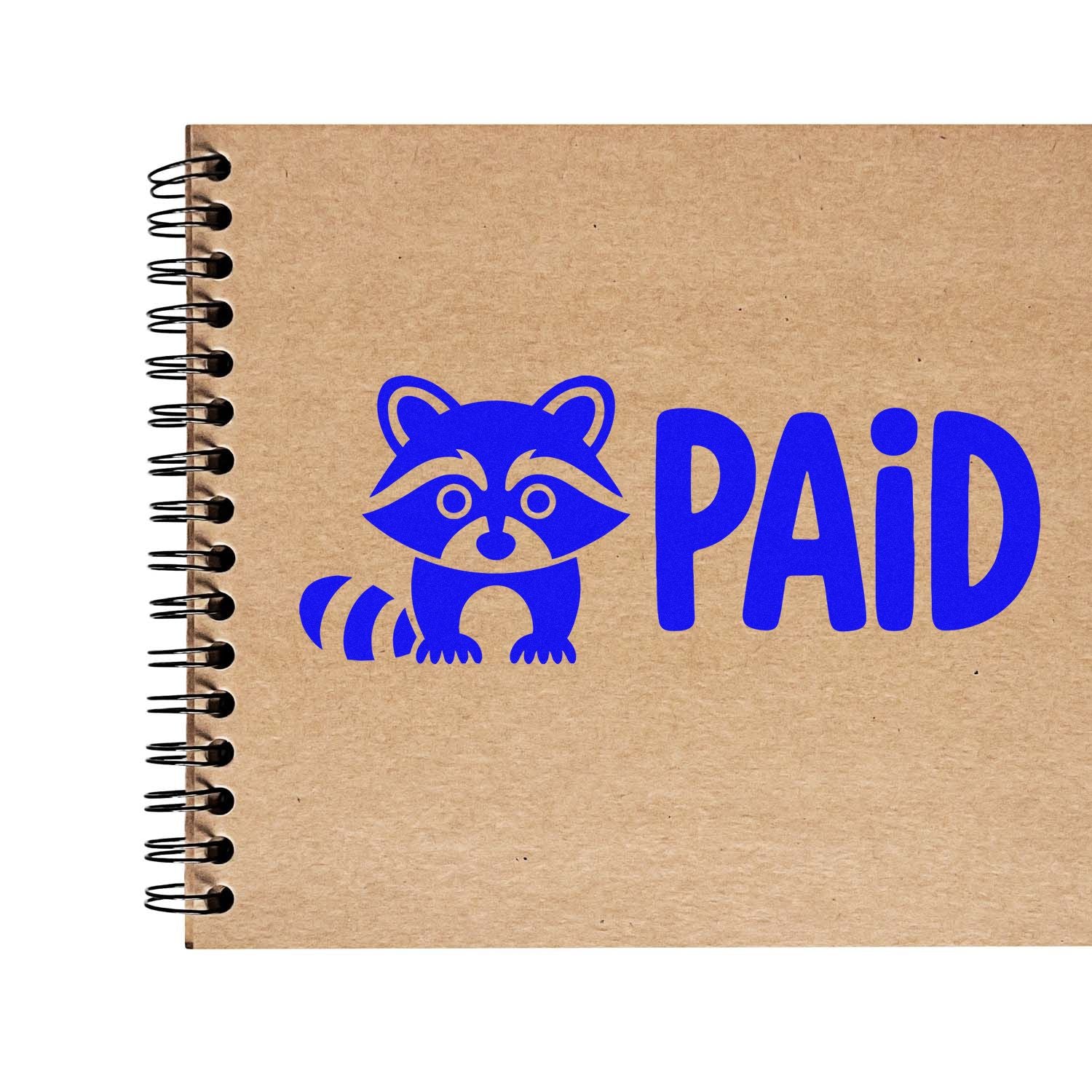 Blue raccoon PAID stamp on tan kraft spiral notebook, showcasing custom stamp and seal branding.