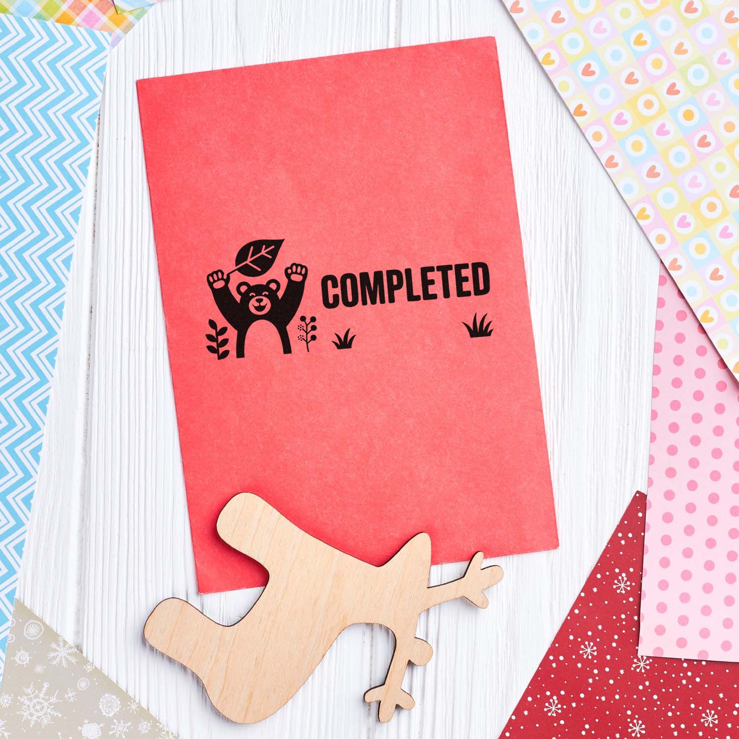Red card with black bear COMPLETED stamp, wooden bear seal, and colorful patterned paper samples.