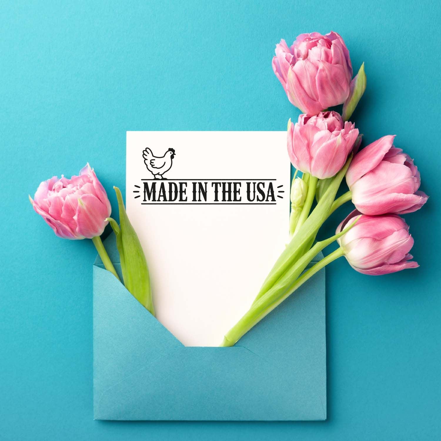 Made in the USA stamp and seal on white card with chicken icon, framed by pink tulips in a blue envelope on turquoise background.