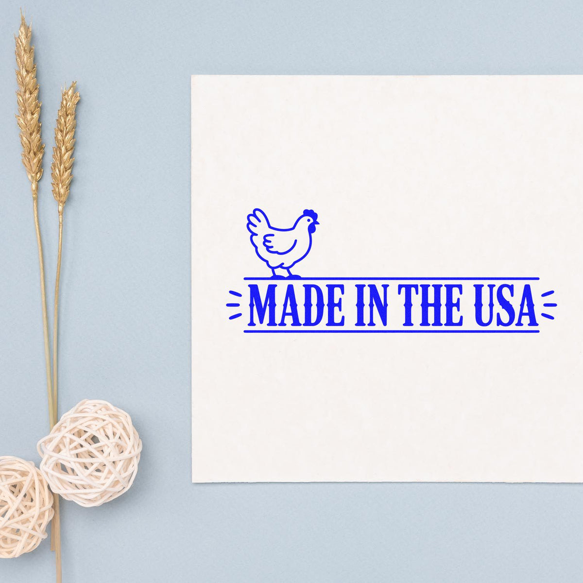 Blue Made in the USA chicken stamp seal on a white card, with pale blue background and wheat stalk decor.