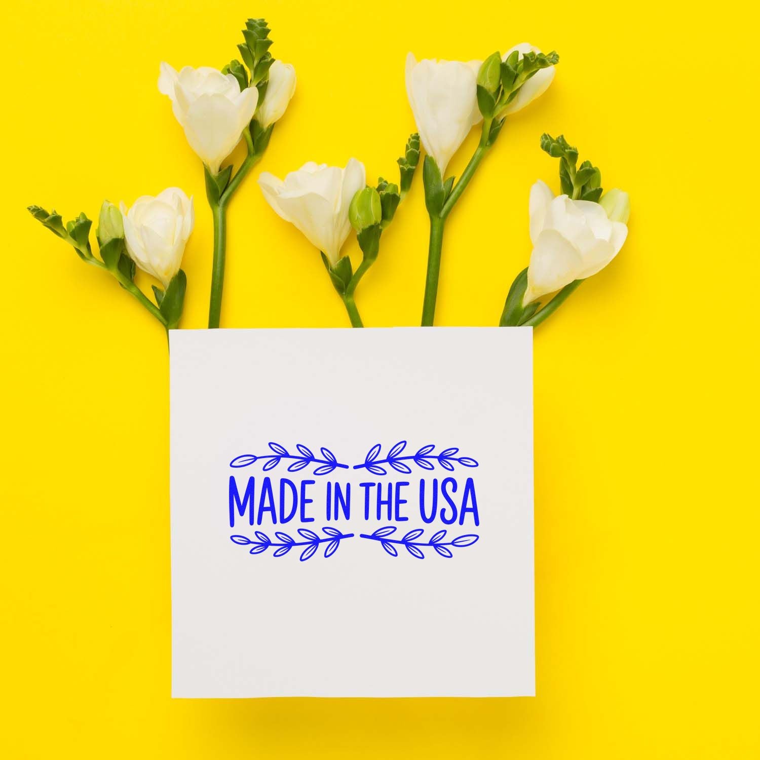 Blue Made in the USA stamp and seal on white paper with white flowers, green stems, on a bright yellow background.