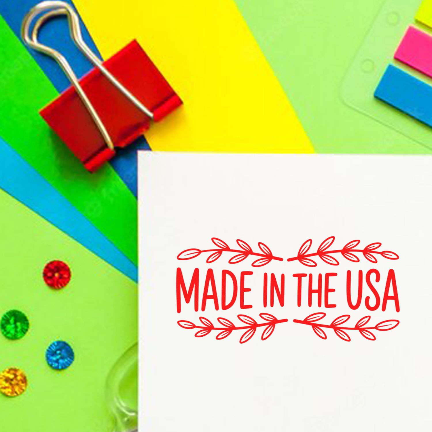 Red Made in the USA stamp on white paper, surrounded by colorful binder clips and seal samples.