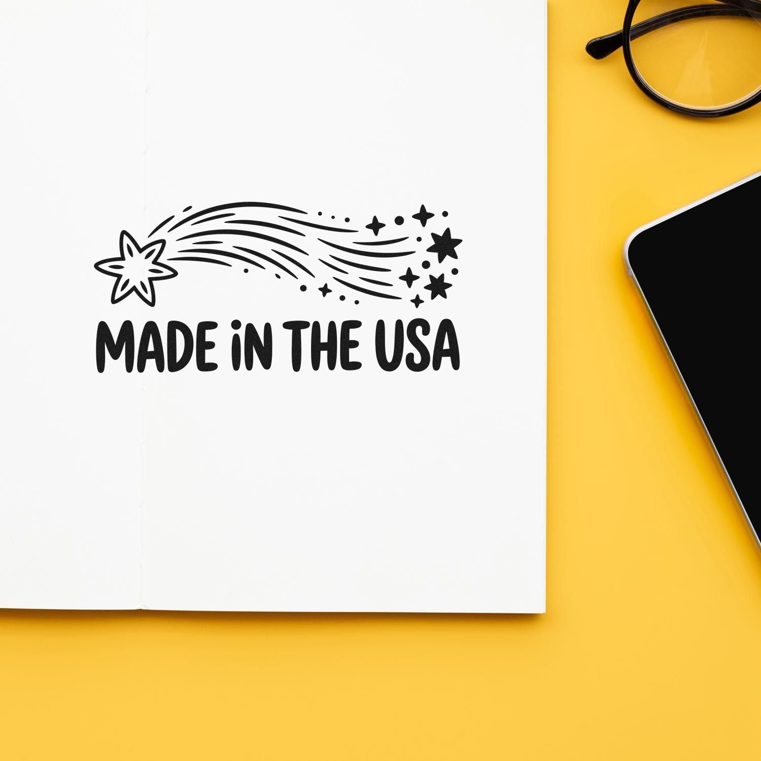 Black Made in the USA stamp with starburst seal on white paper, on a yellow background beside black glasses and phone.
