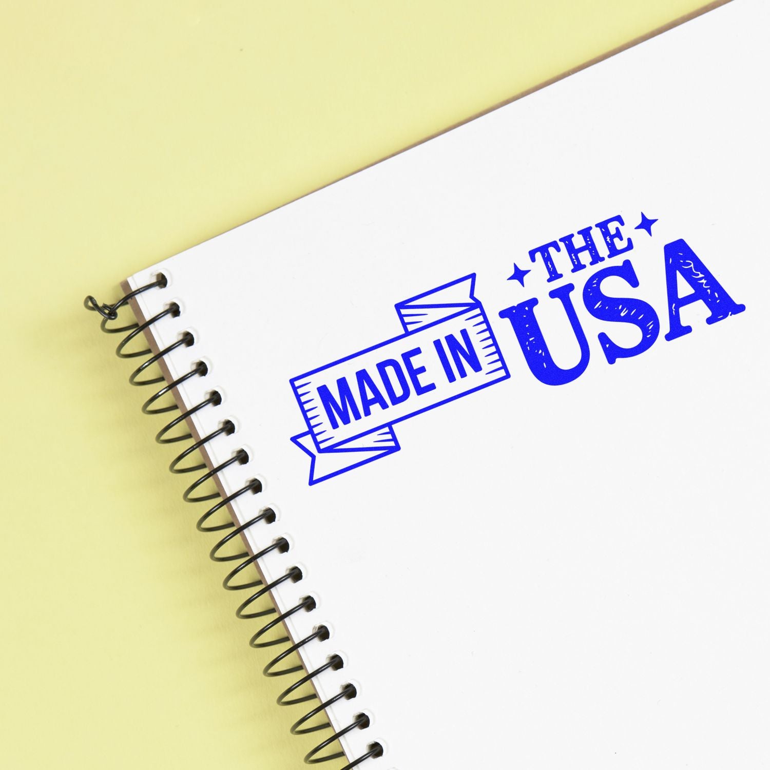 Blue MADE IN USA stamp-style seal on a white spiral notebook over a pale yellow background.
