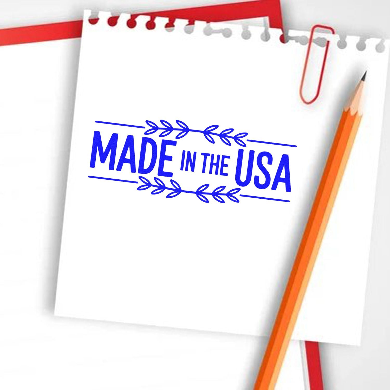 Blue Made in the USA stamp seal on white notepad, with red paperclip and orange pencil.