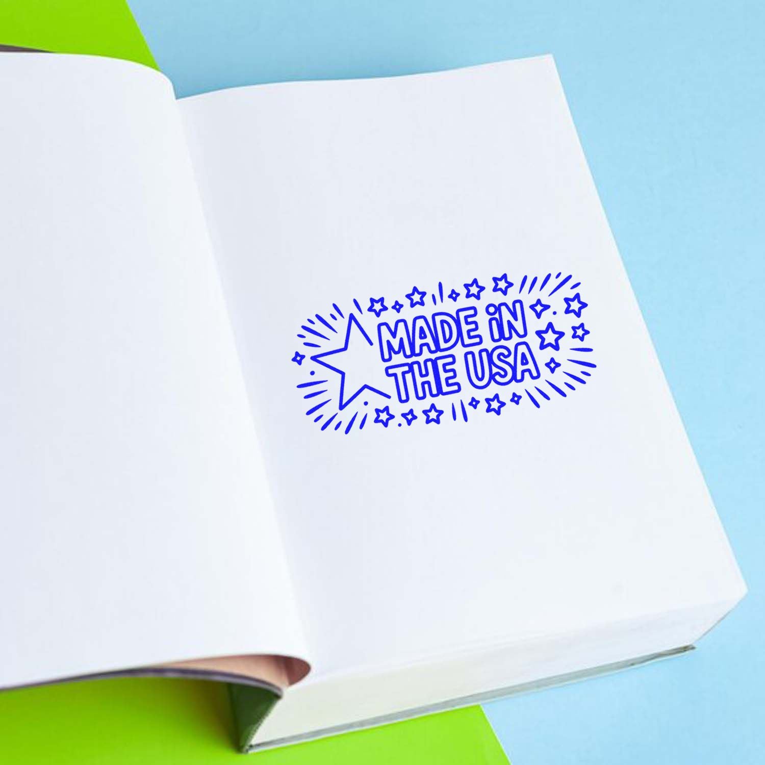Blue Made in the USA stamp seal with stars on an open white notebook, set against a light blue and green background.