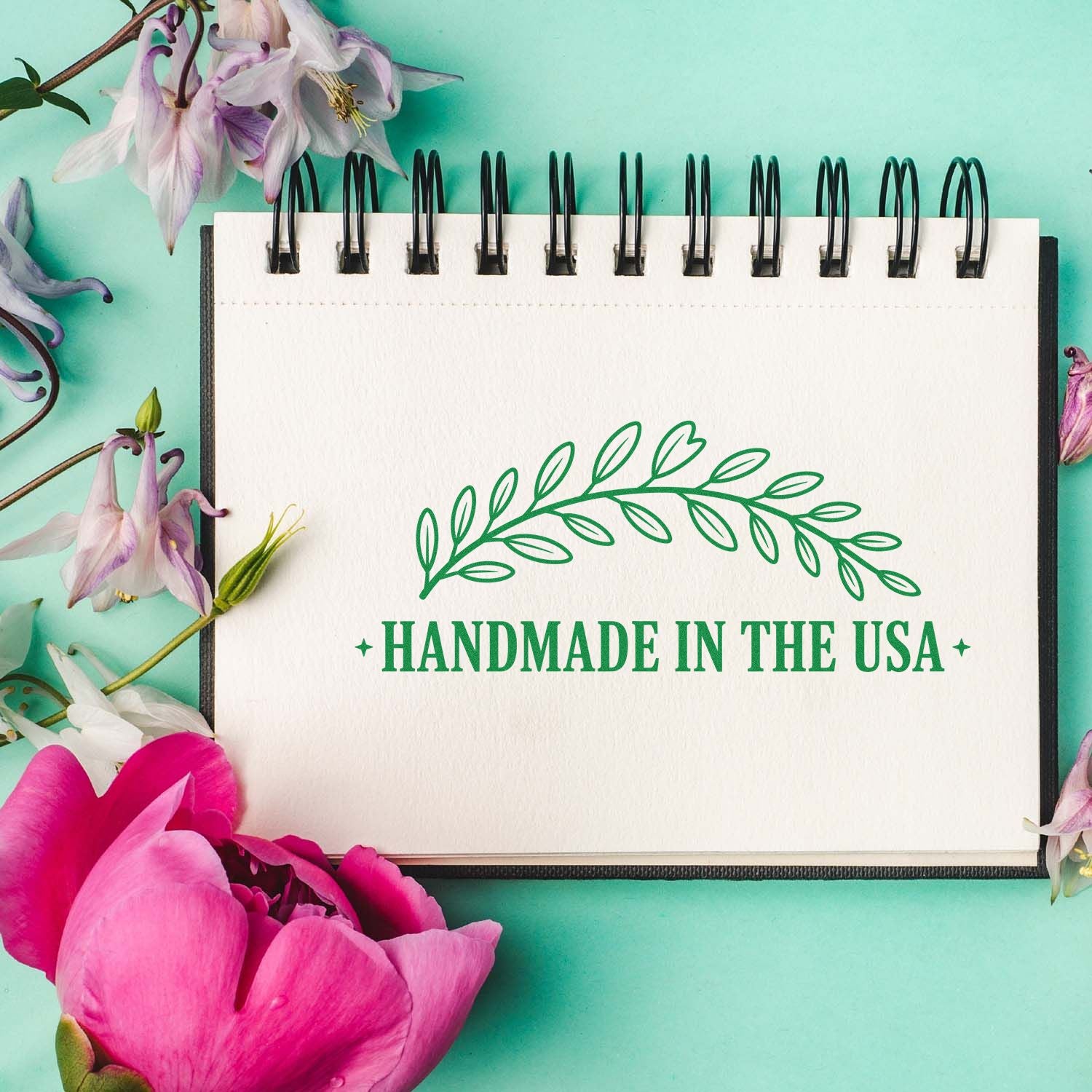 Green handmade in the USA stamp seal on a white spiral notebook, with pink and purple flowers on a mint background.