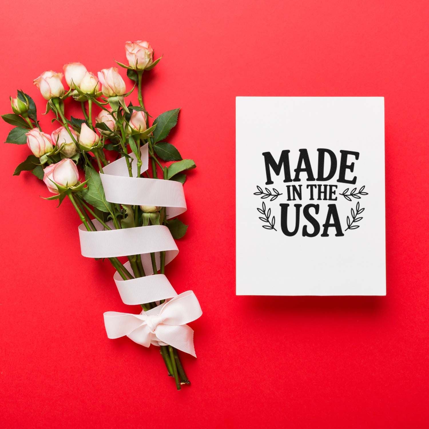 Pink roses tied with white ribbon beside a white card with a black Made in the USA stamp seal on a red background.